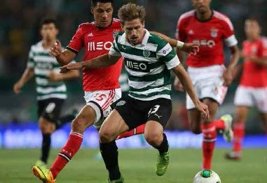 Soccer players in red and green-and-white striped uniforms competing for the ball during a match