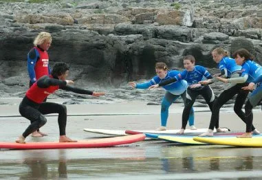 Surf instructors and beginners practicing balance on paddleboards near a rocky shoreline