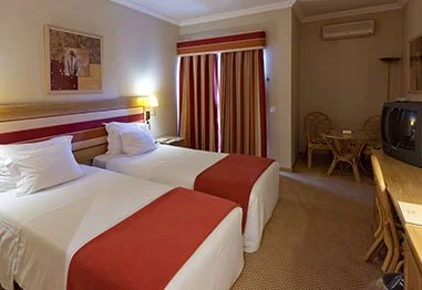 Hotel room with two twin beds, red-and-white bedding, striped curtains, television, and desk