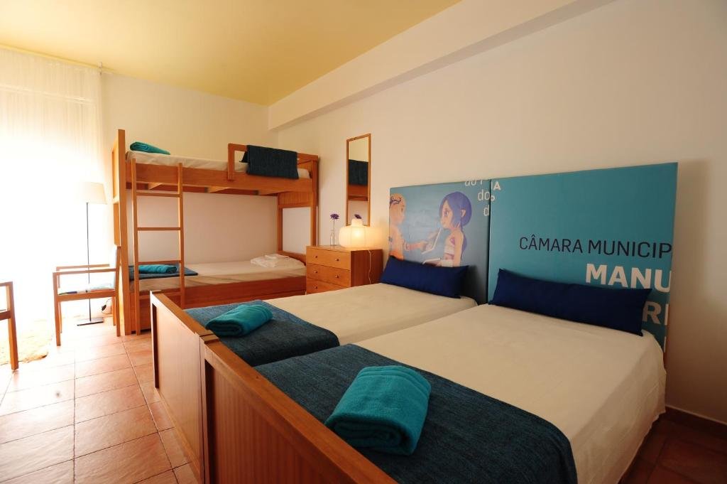 Bright hostel room with a double bed, wooden bunk beds, turquoise towels, and colorful wall artwork.