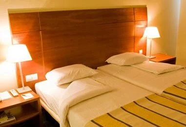 Hotel room with twin beds, white linens, wooden headboard, bedside tables, and lamps