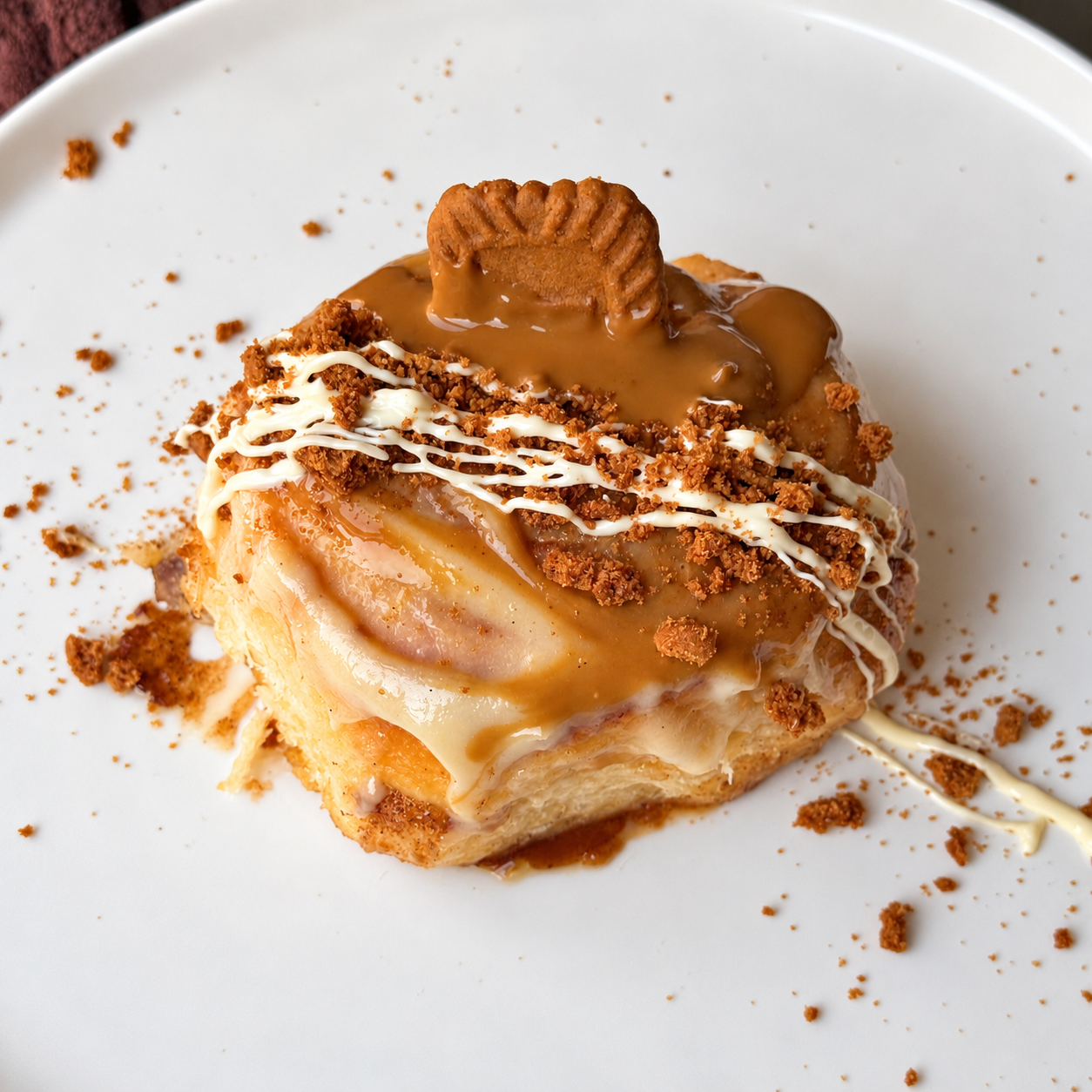 A dessert with apple slices, caramel sauce, whipped cream, crushed cookies, and a whole cookie on top, served on a white plate.