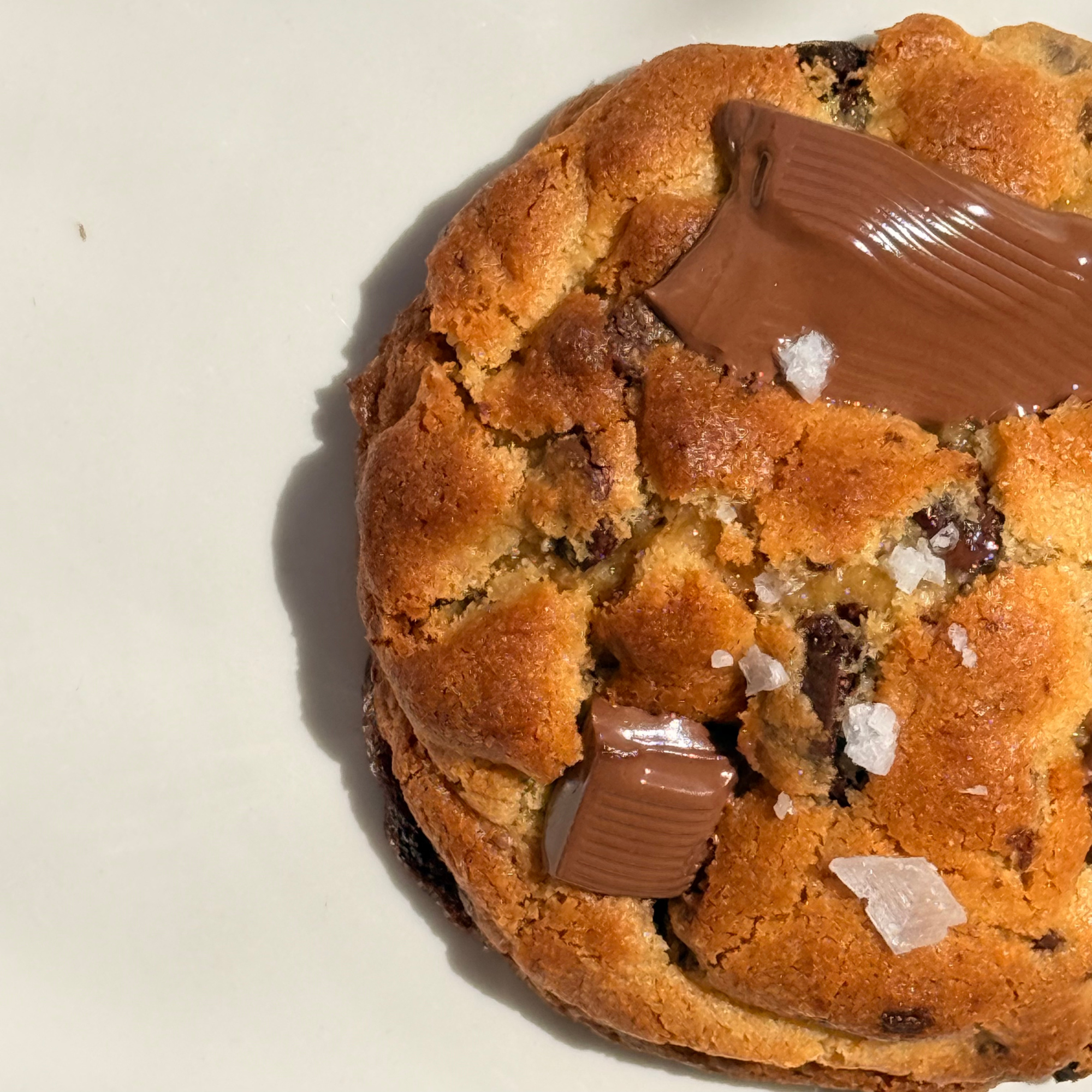 Close-up of a partially sliced chocolate chip muffin on a white surface, with salt crystals on top.
