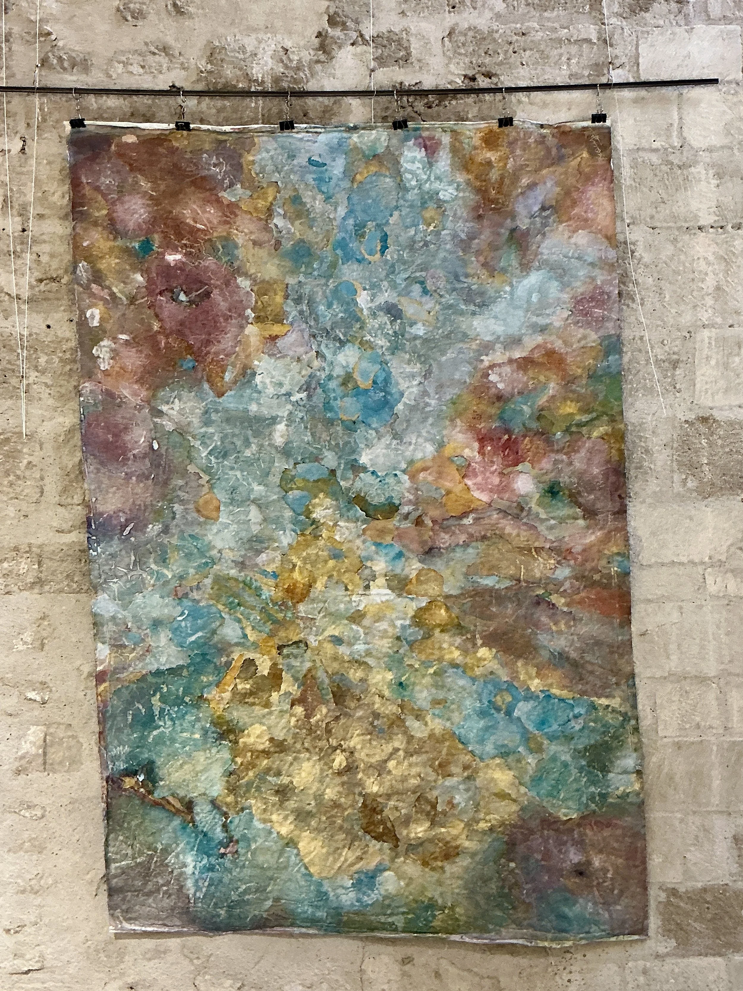 Peinture abstraite avec des couleurs pastel, des touches de blanc, de bleu, de rose, de jaune et de vert, montée sur un mur en pierre.