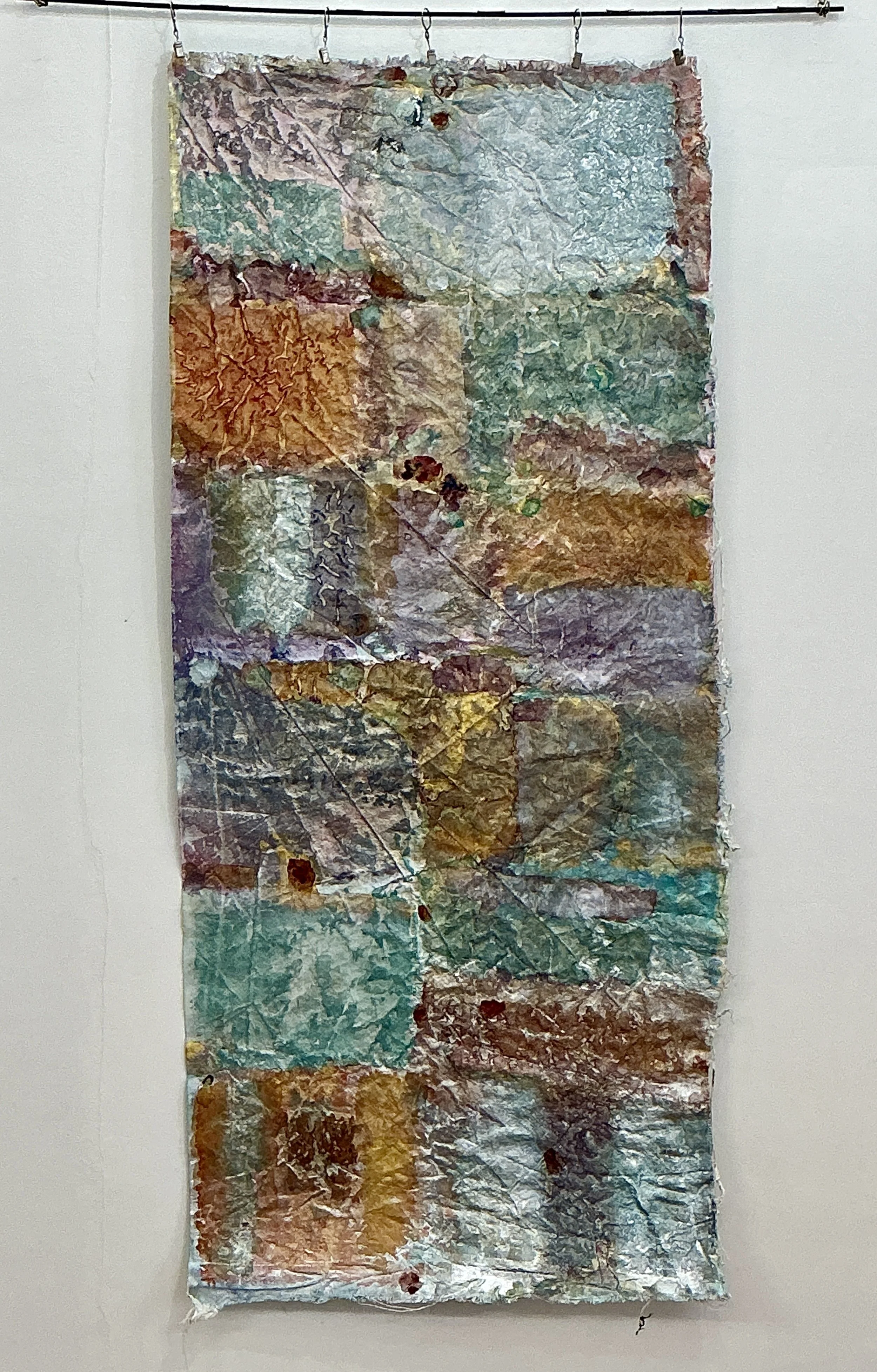 Une œuvre d'art abstraite avec différentes textures et couleurs, suspendue à un mur blanc.