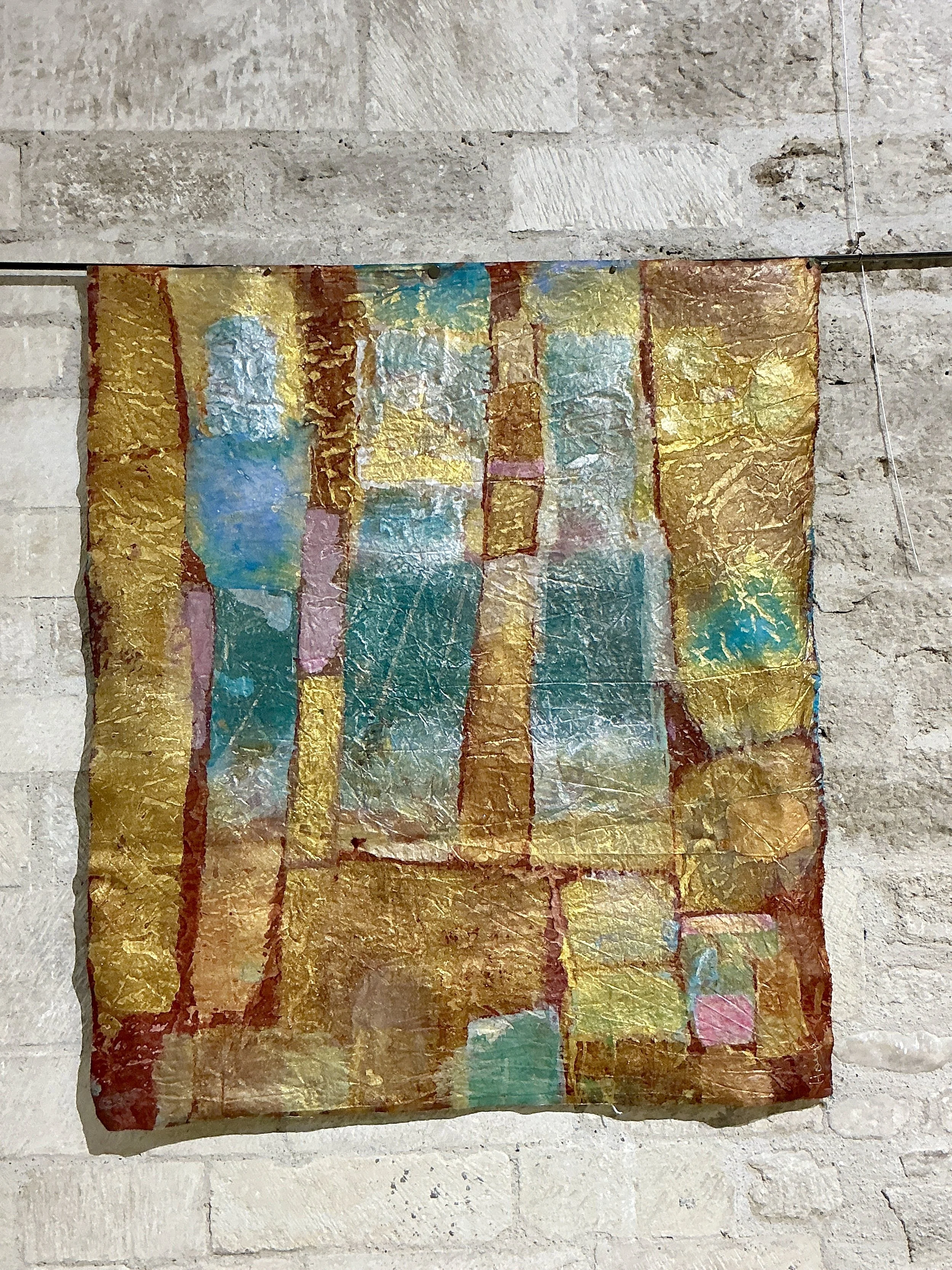 Une œuvre d'art abstraite avec des couleurs vives, principalement or, avec des touches de bleu, rose et blanc, sur un fond en papier ou toile.