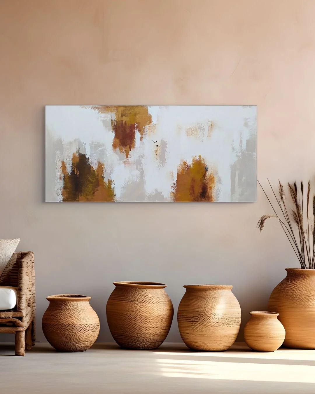 A living room scene with a large, horizontal abstract painting on a beige wall, six wooden vases of varying sizes arranged on the floor, a partial wicker chair with white cushion on the left, and dried grass in a tall terracotta pot on the right.