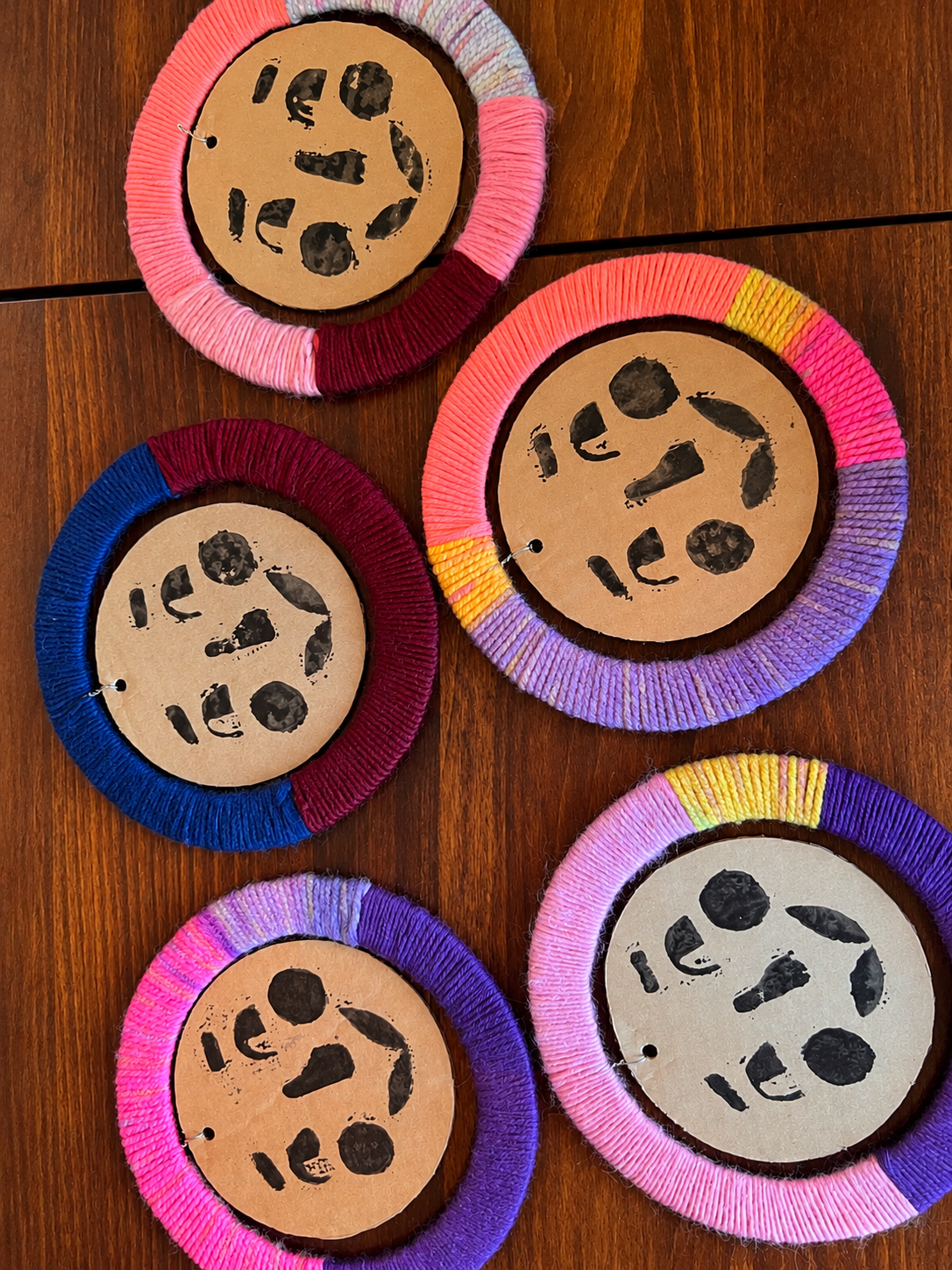 Colorful circular craft projects with yarn borders and painted animal faces on cardboard, arranged on a wooden surface.