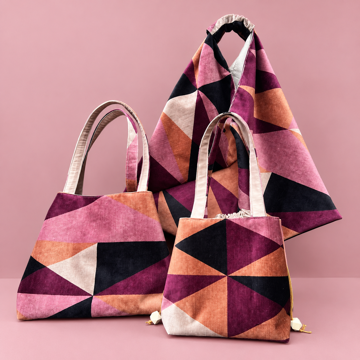Three geometric-patterned fabric bags with pink, black, orange, and white shapes, set against a pink background.