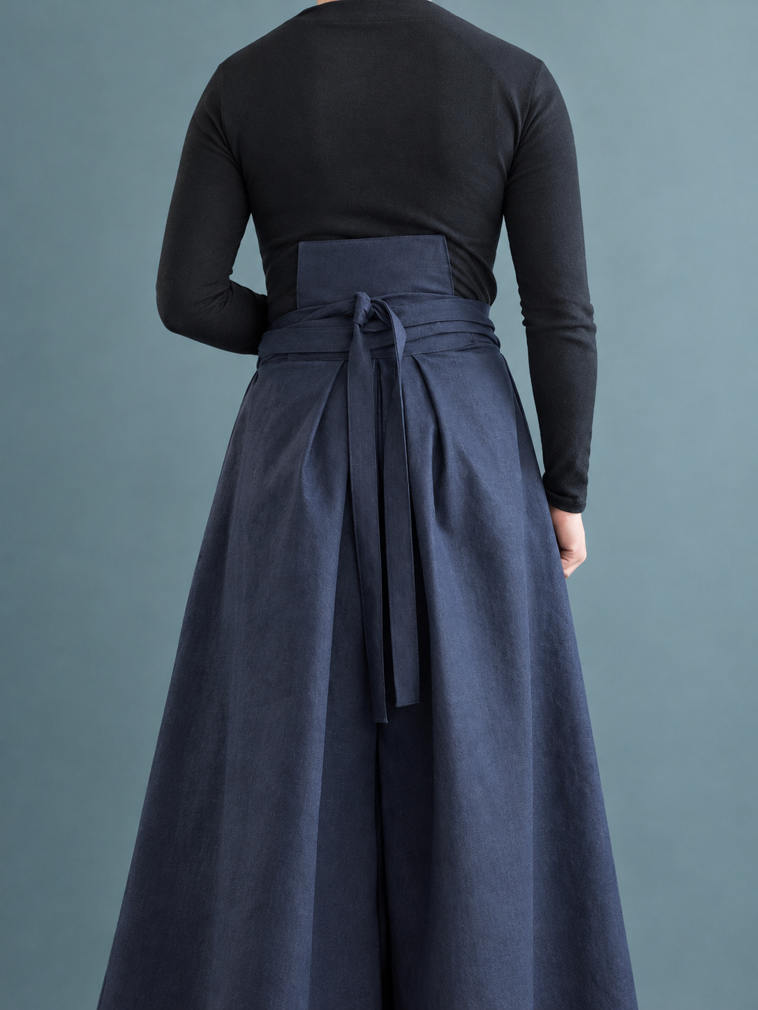 Person wearing a black long-sleeve shirt and a navy blue high-waisted, wide-leg skirt with a tied waist.