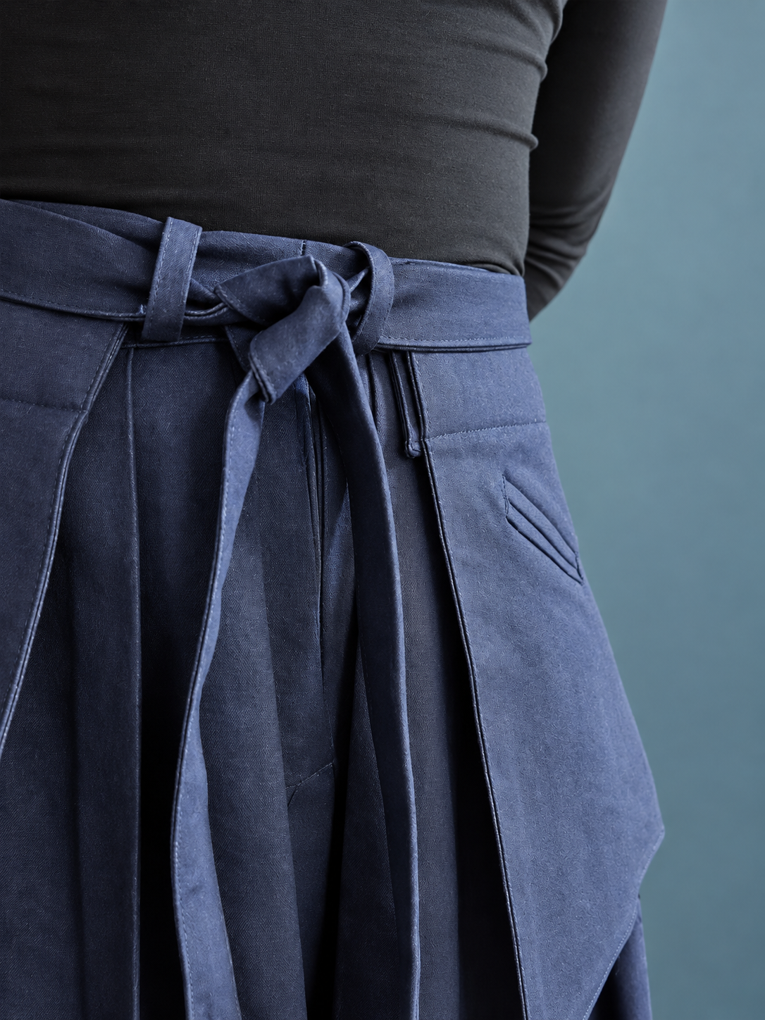Close-up of high-waisted navy blue pants with a fabric belt tied in a bow and a top with long sleeves.