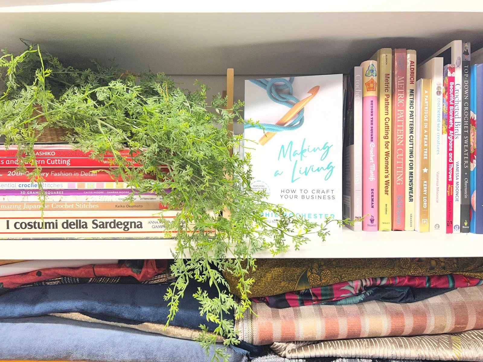 Bookshelf with crochet books, a green plant, and a book titled "Making a Living."