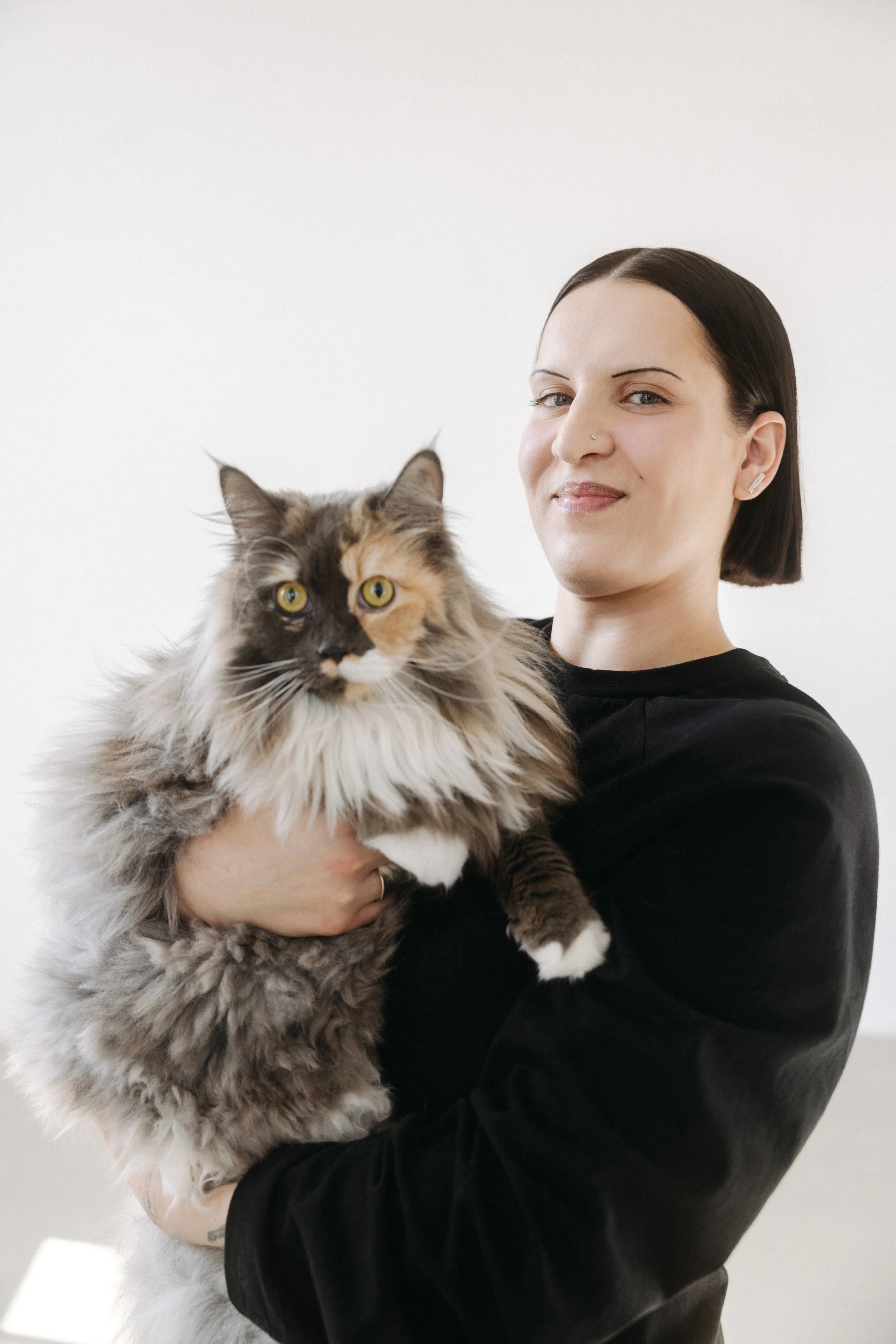 Frau in schwarzem Oberteil hält eine langhaarige graue Katze im Arm.
