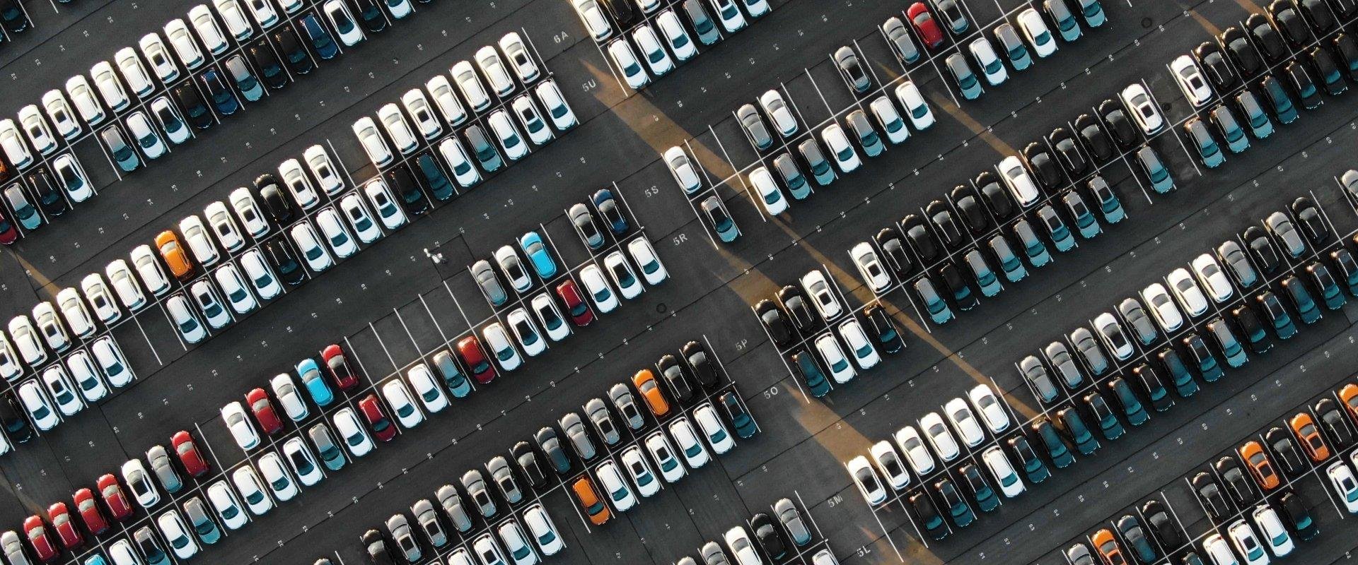 Automobile - Une vue aérienne d'un grand parking rempli de voitures de différentes couleurs, organisées en rangées.