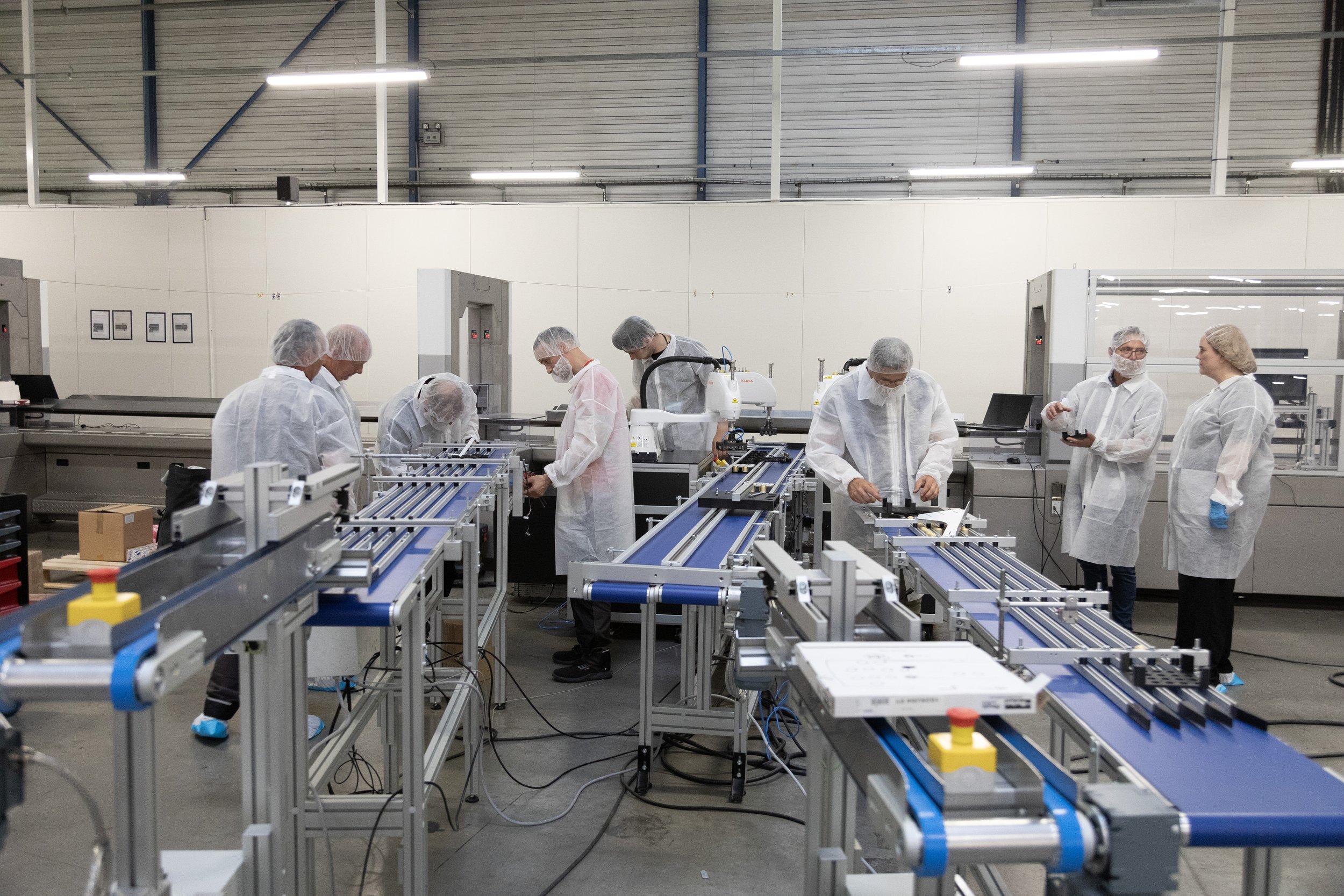 Une salle blanche dans une usine avec des personnes en blouse et coiffes de protection autour de machines de production.