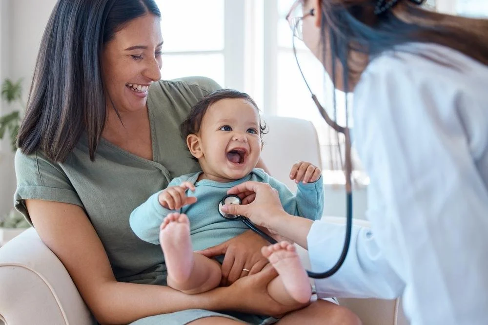 Une mère souriante avec un bébé qui rit, un médecin utilise un stéthoscope pour écouter le cœur de l'enfant.