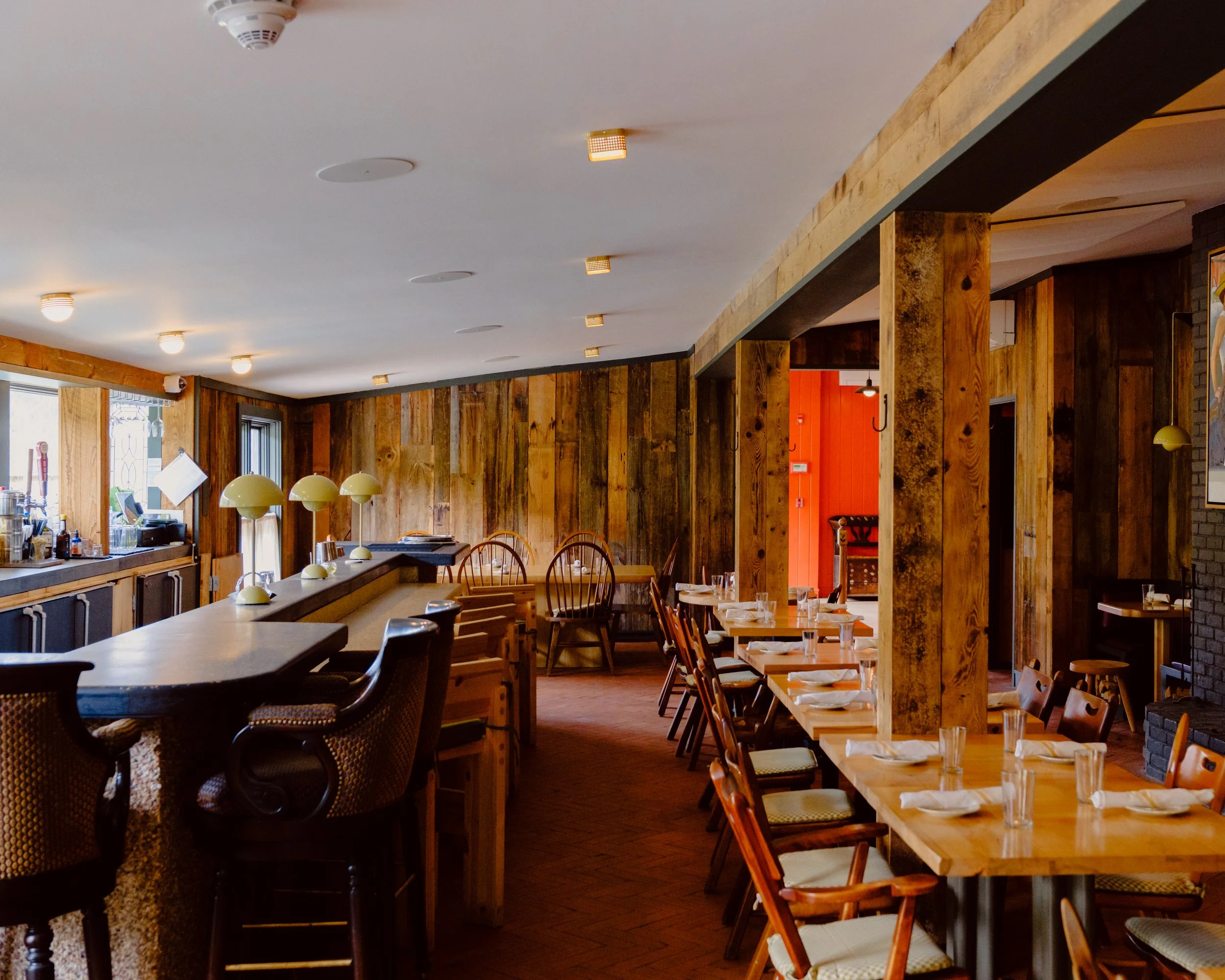 A cozy restaurant interior with wooden walls, tables set with glasses and napkins, and warm lighting.