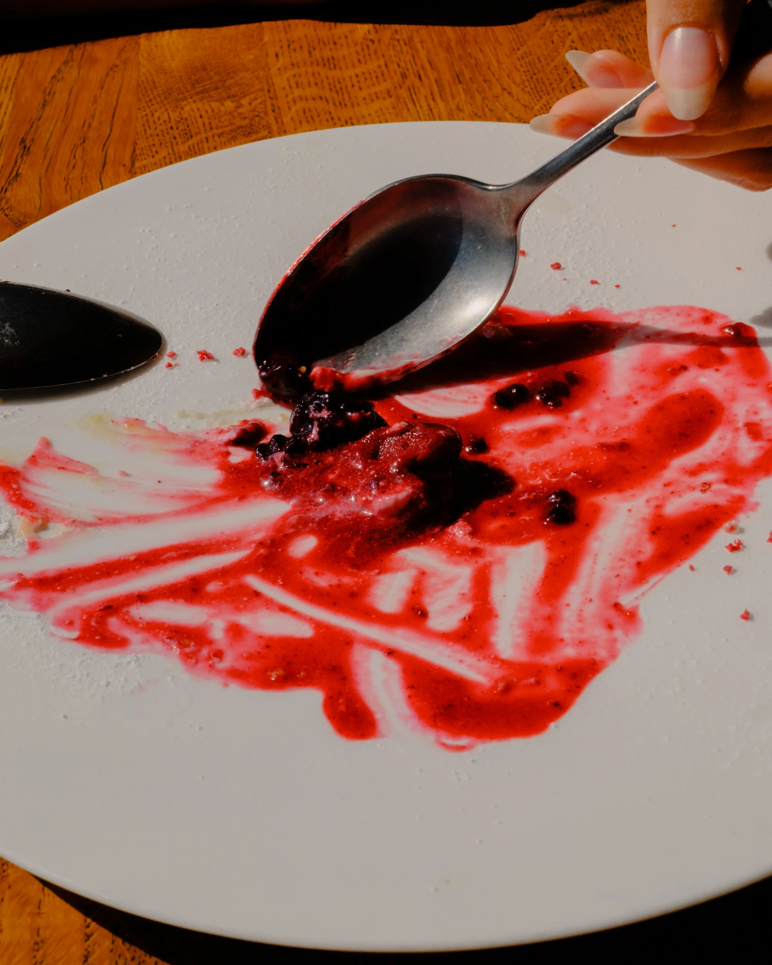 A white plate with remnants of a berry sauce and scattered berries, some smears of red sauce, on a wooden table.