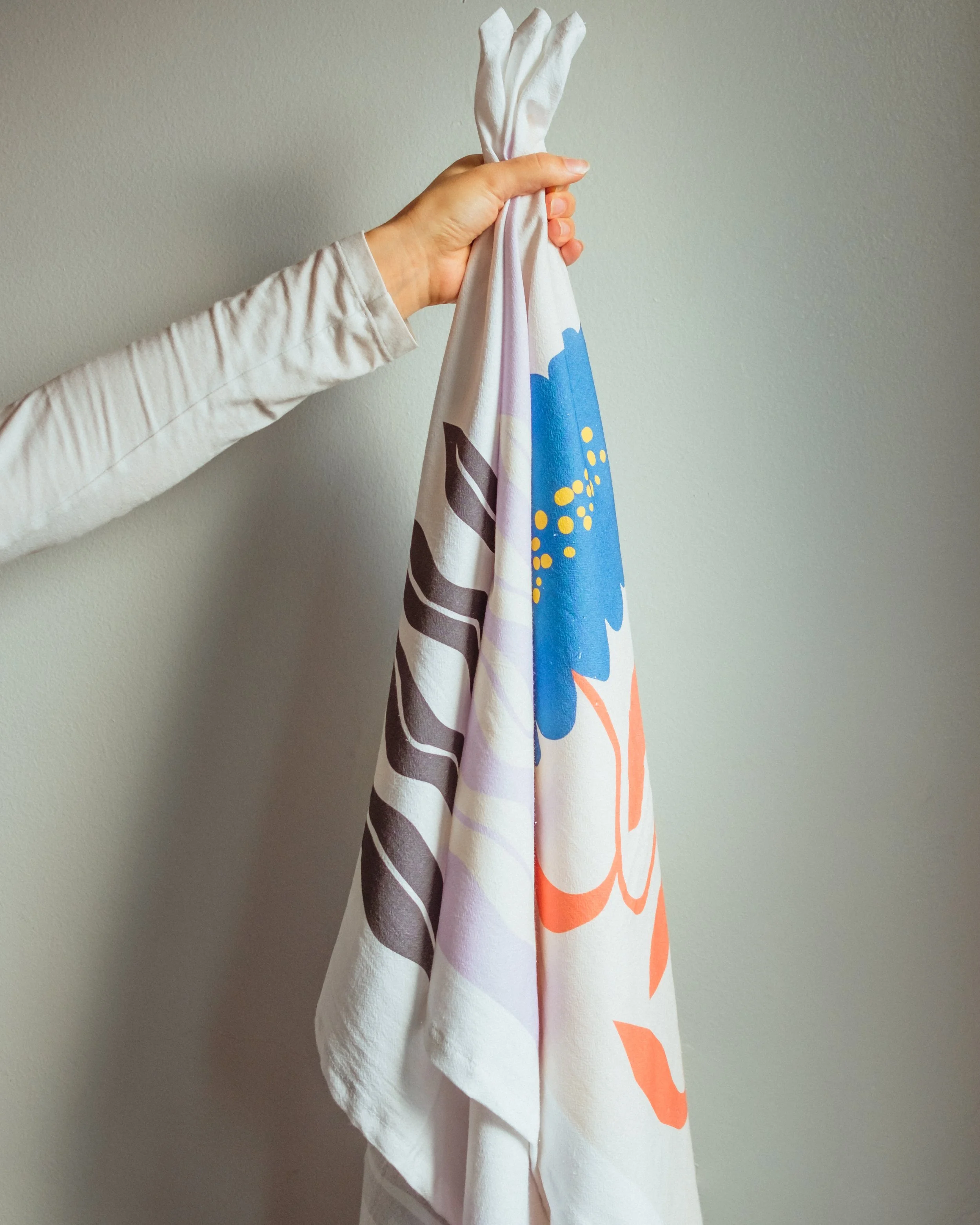Close-up of a hand holding a white cloth with a colorful, abstract pattern against a plain wall.