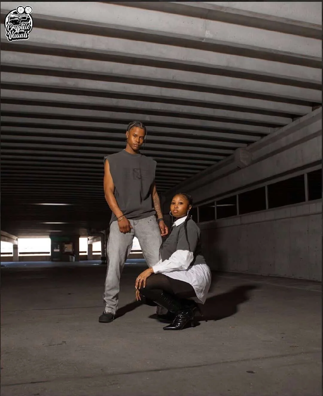 A man and a woman in urban fashion posing in an underground parking garage.