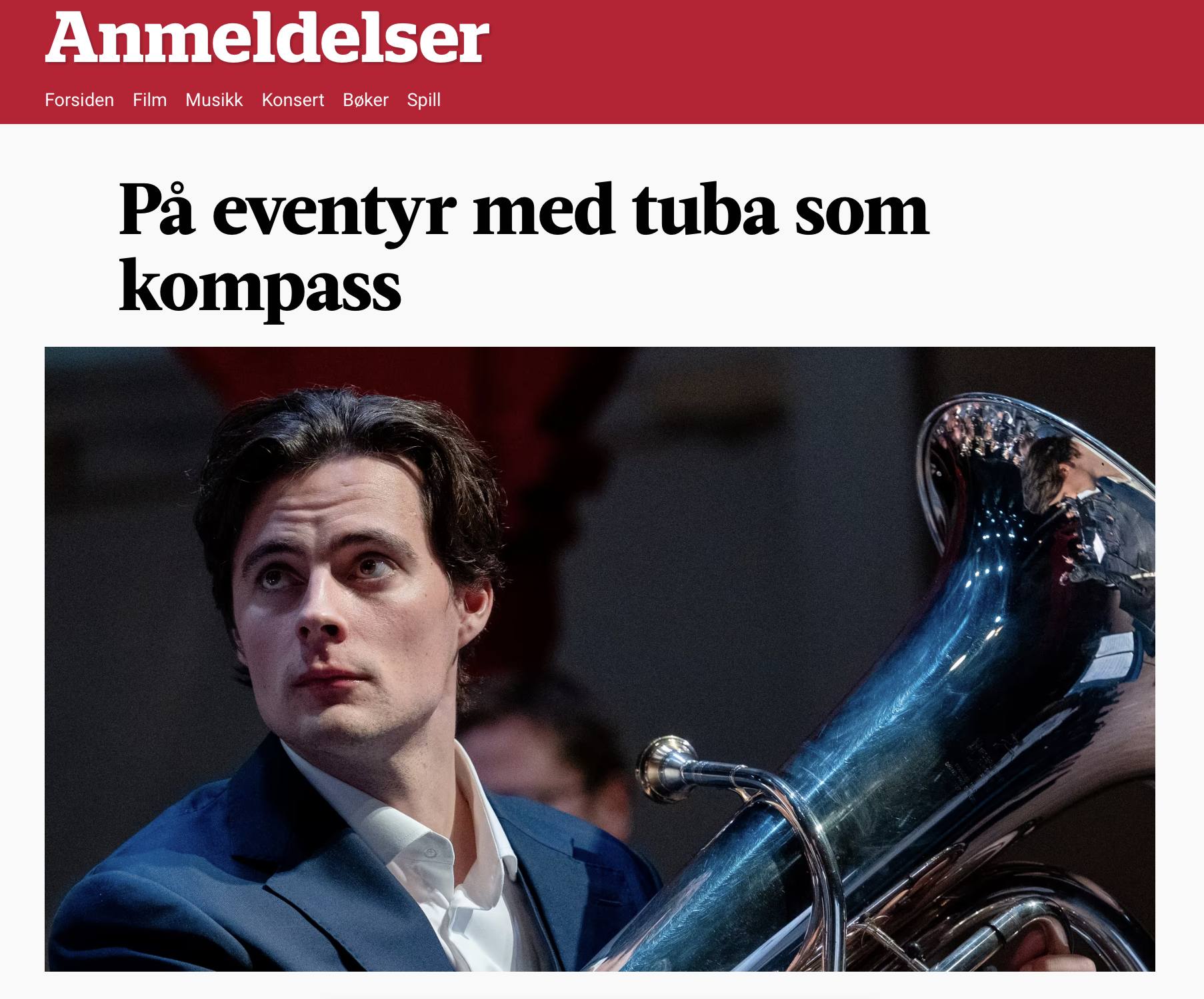 A man in a blue suit playing a tuba, looking up, at what appears to be a formal event or concert.