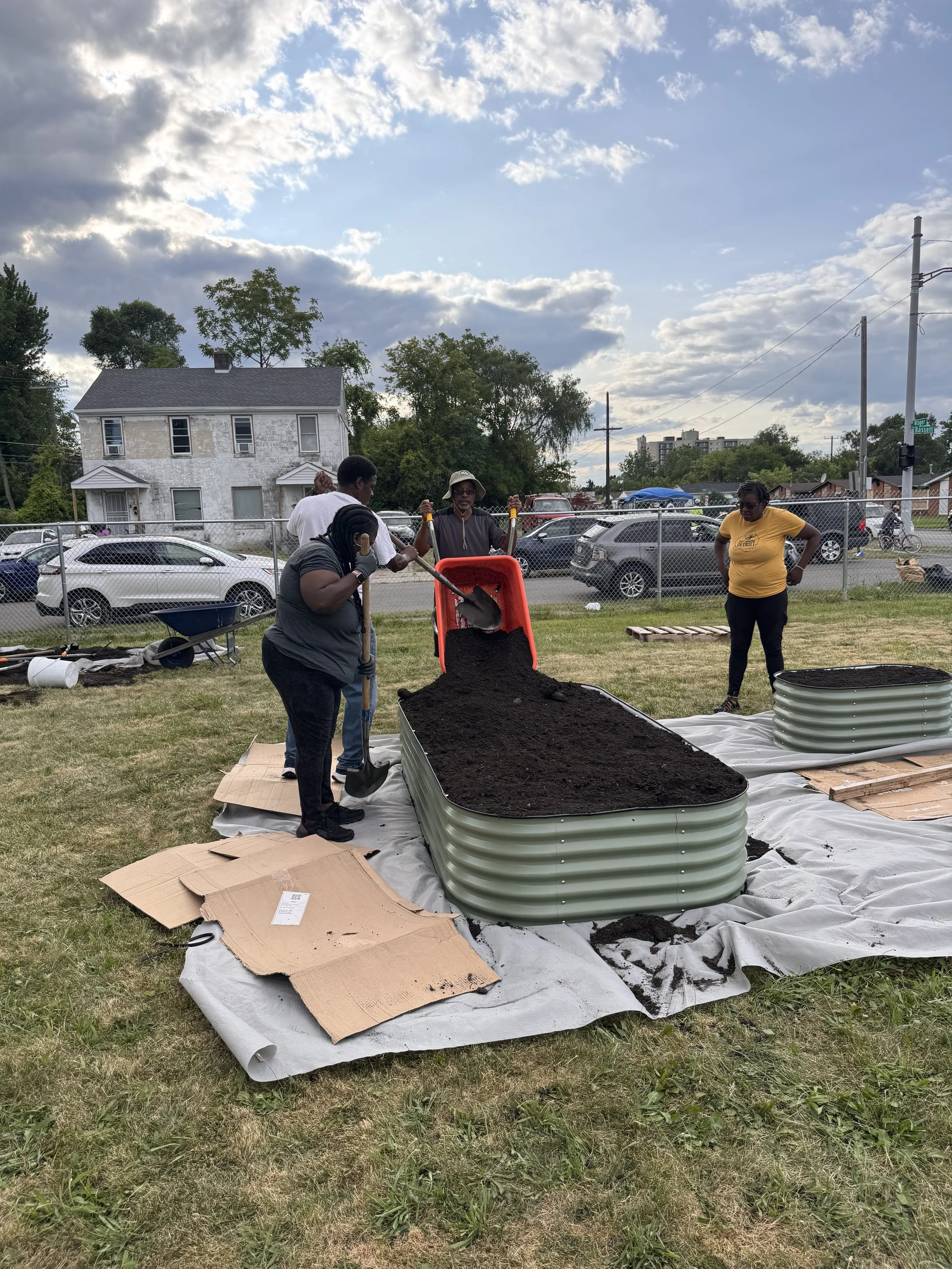 Four people adding soil to a metal raised bed at an urban garden in Southwest Detroit