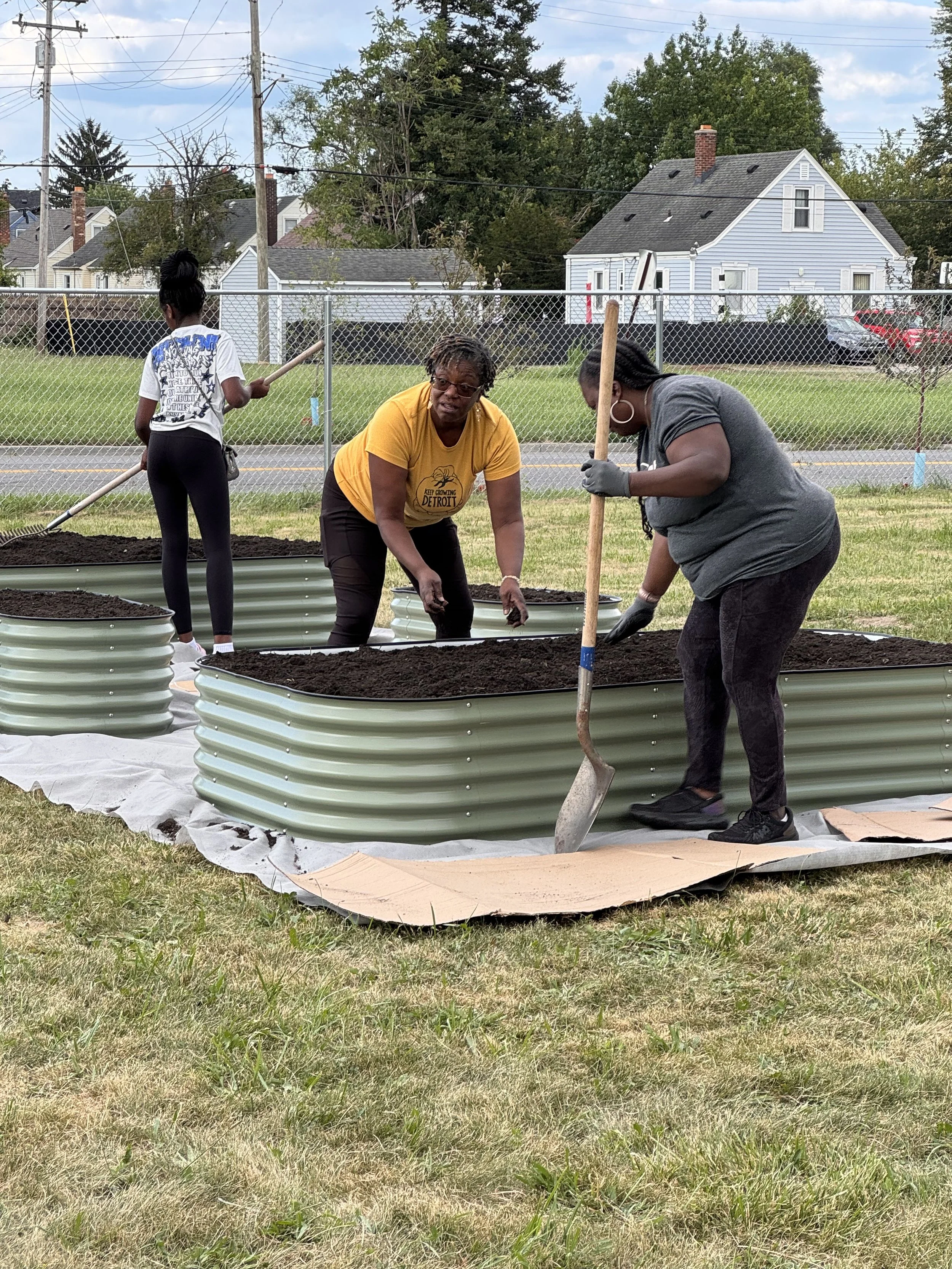 Three people filling metal raised beds with planting soil