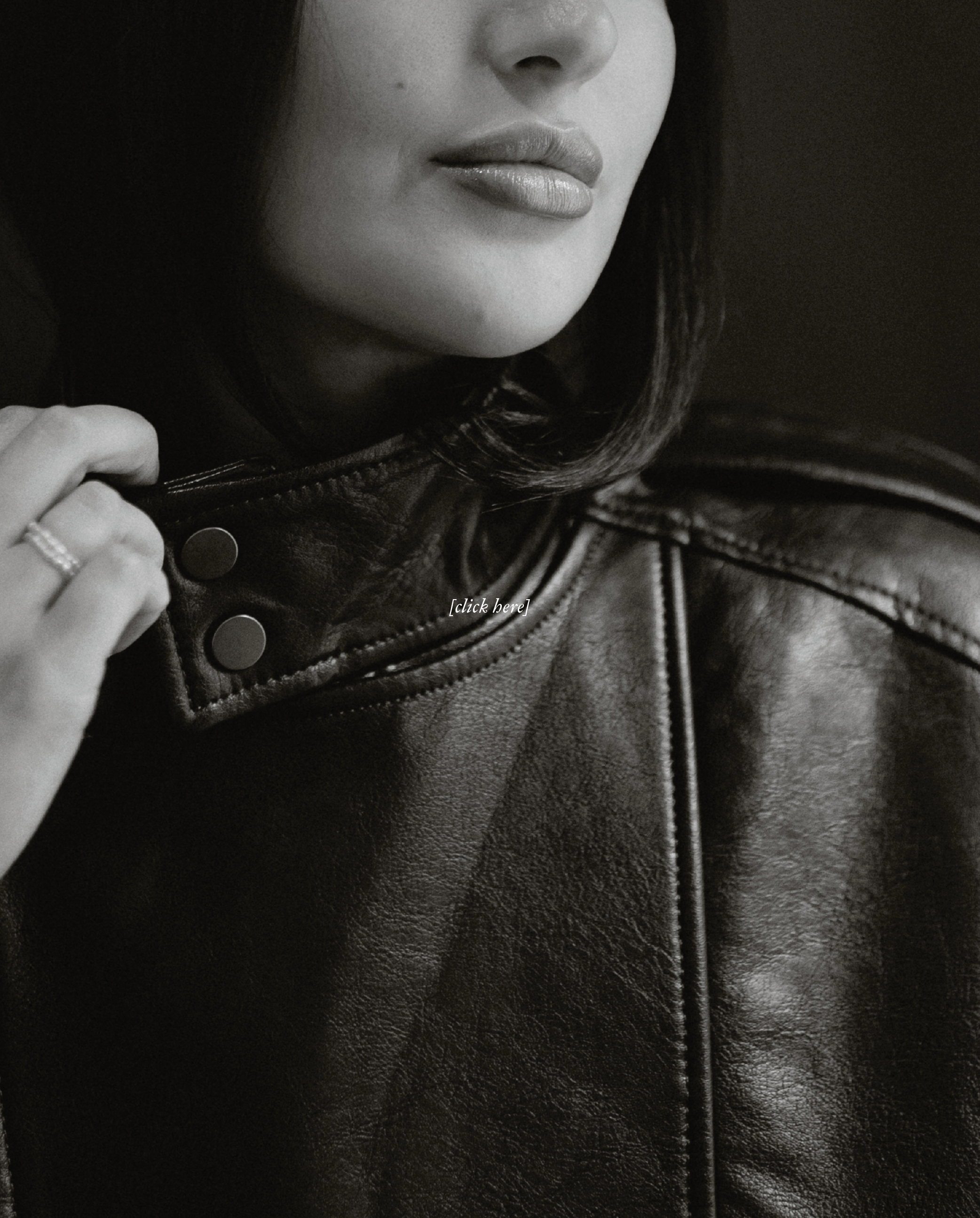 Close-up of a woman in black and white, showing her lips, nose, and part of her face, with her hand wearing a ring on the finger holding a leather jacket collar.