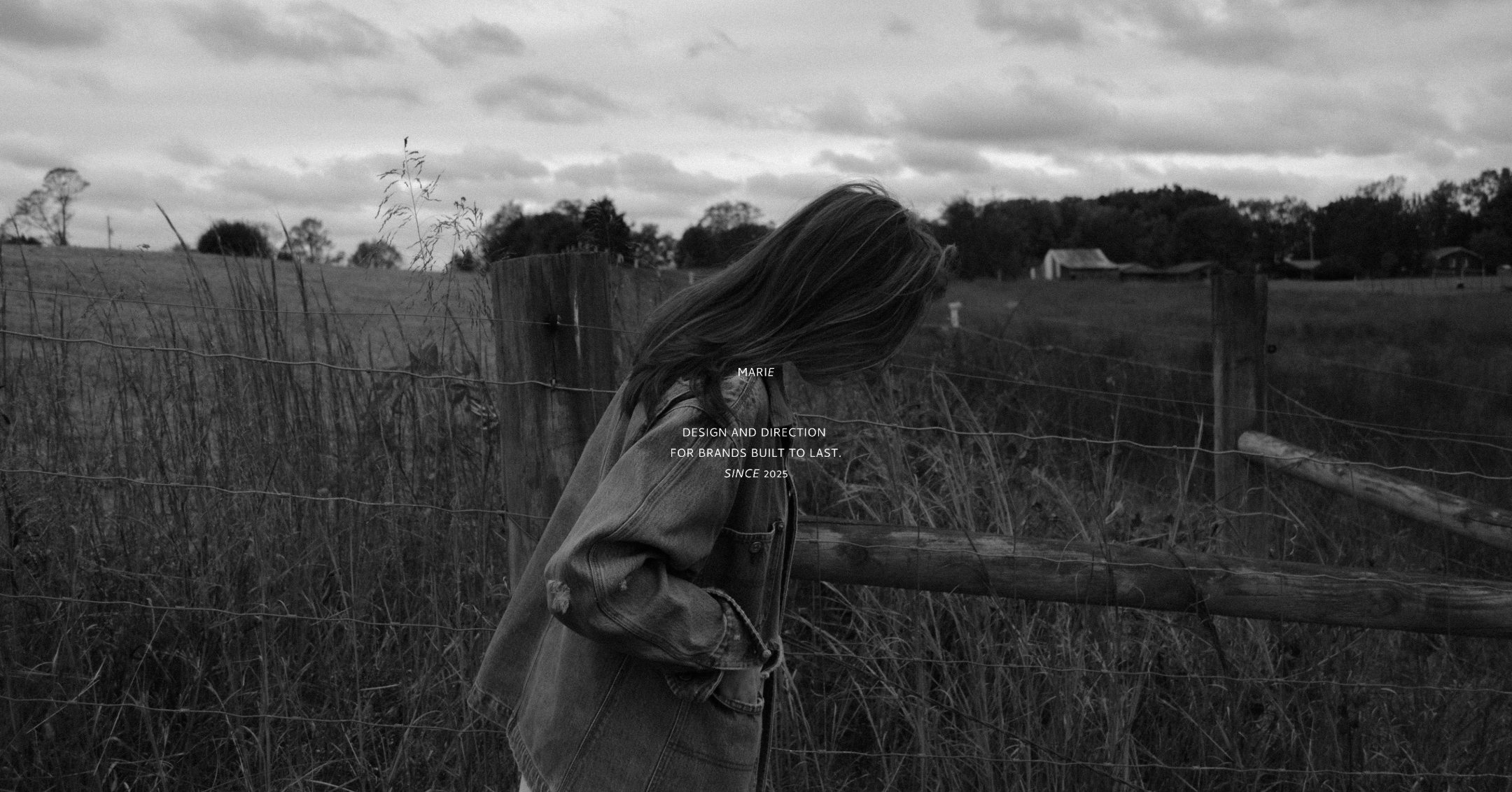 A black and white photo of a girl with long hair looking downward while leaning on a wooden fence in a rural field with trees and houses in the background. Overlaid text reads: "Marie, Design and Direction for brands built to last. Since 2025."