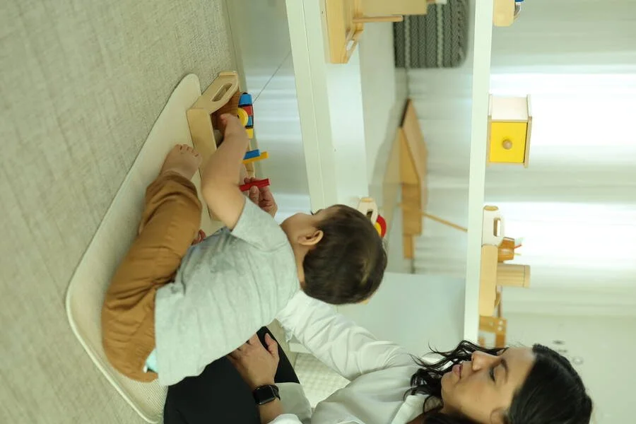 Criança explorando materiais Montessori acompanhada por um adulto.
