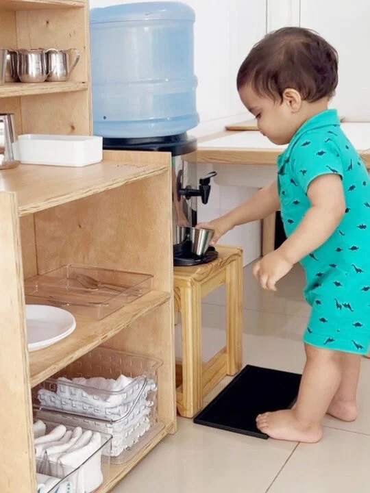 Criança servindo água em ambiente Montessori preparado para atividades de vida prática.