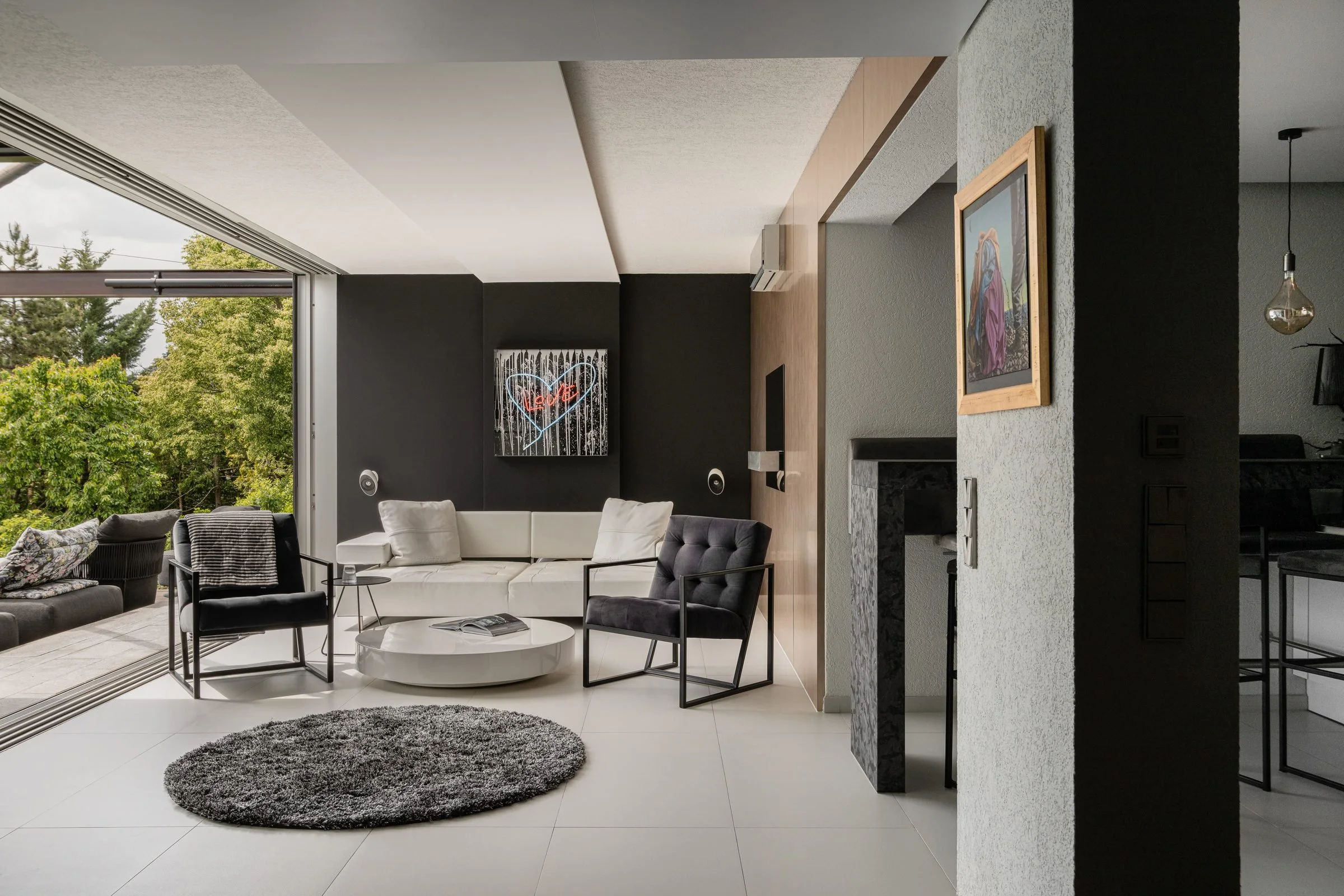 Ein modernes Wohnzimmer mit großen Glasfenstern, grauem Teppich, weißem Sofa, schwarzen Sesseln und einer runden weißen Couch.