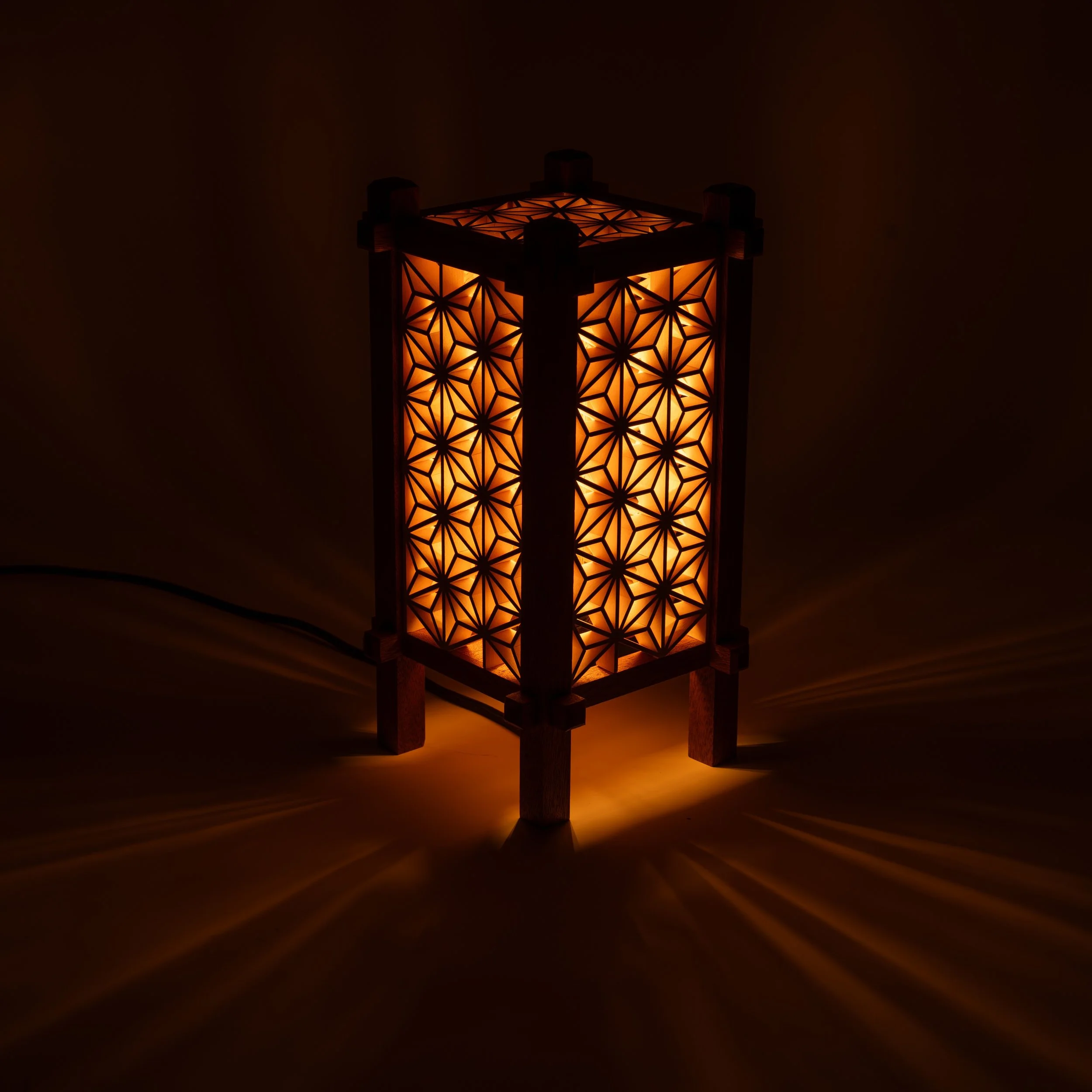 De handgemaakte Yoake-lamp verspreidt warm licht en projecteert geometrische schaduwen door het Kumiko-patroon.