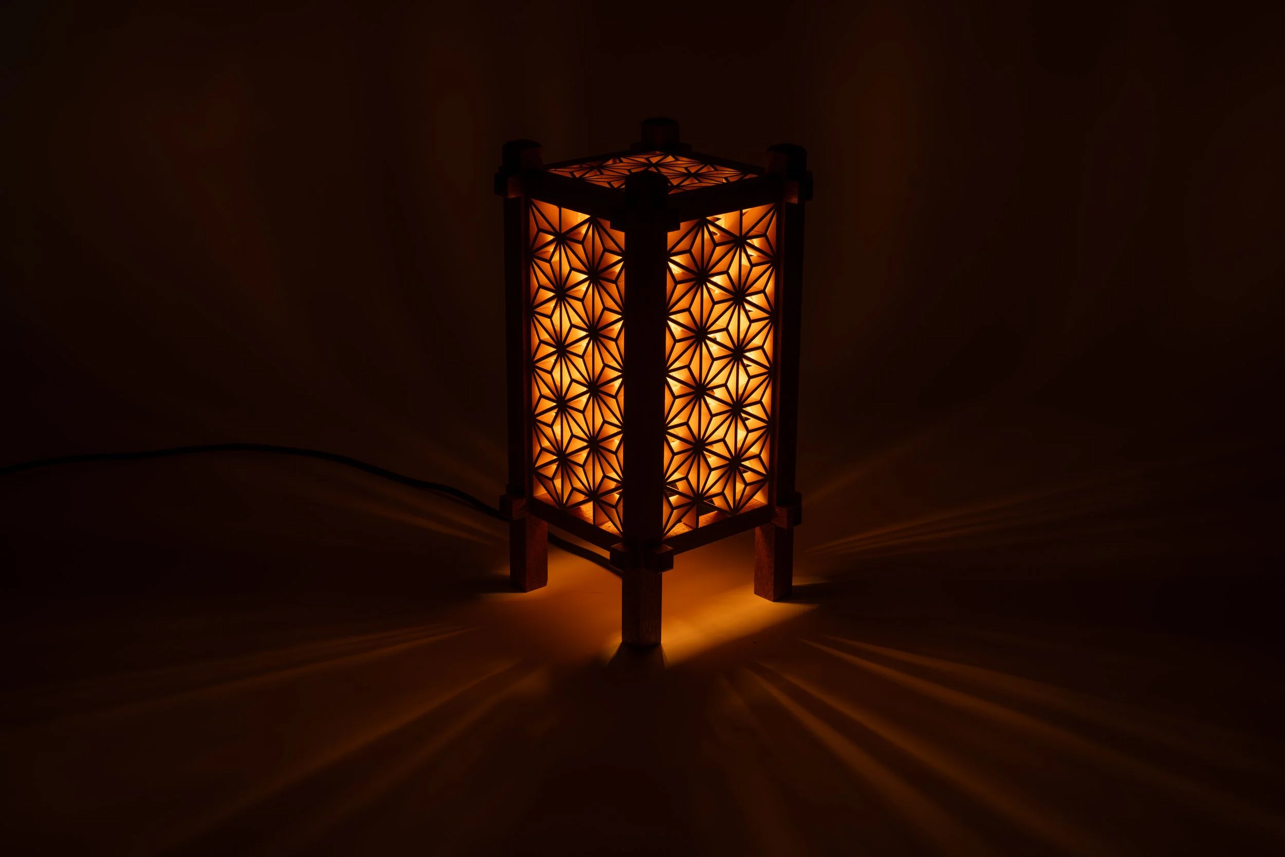 De handgemaakte Yoake-lamp verspreidt warm licht en projecteert geometrische schaduwen door het Japanse Kumiko-patroon.