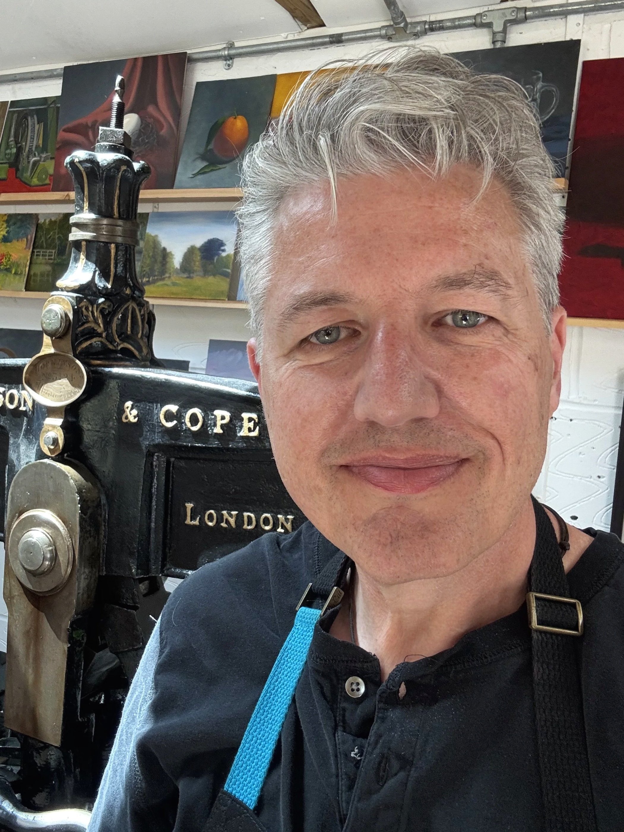 Man posing beside an antique Albion press in an art-filled studio