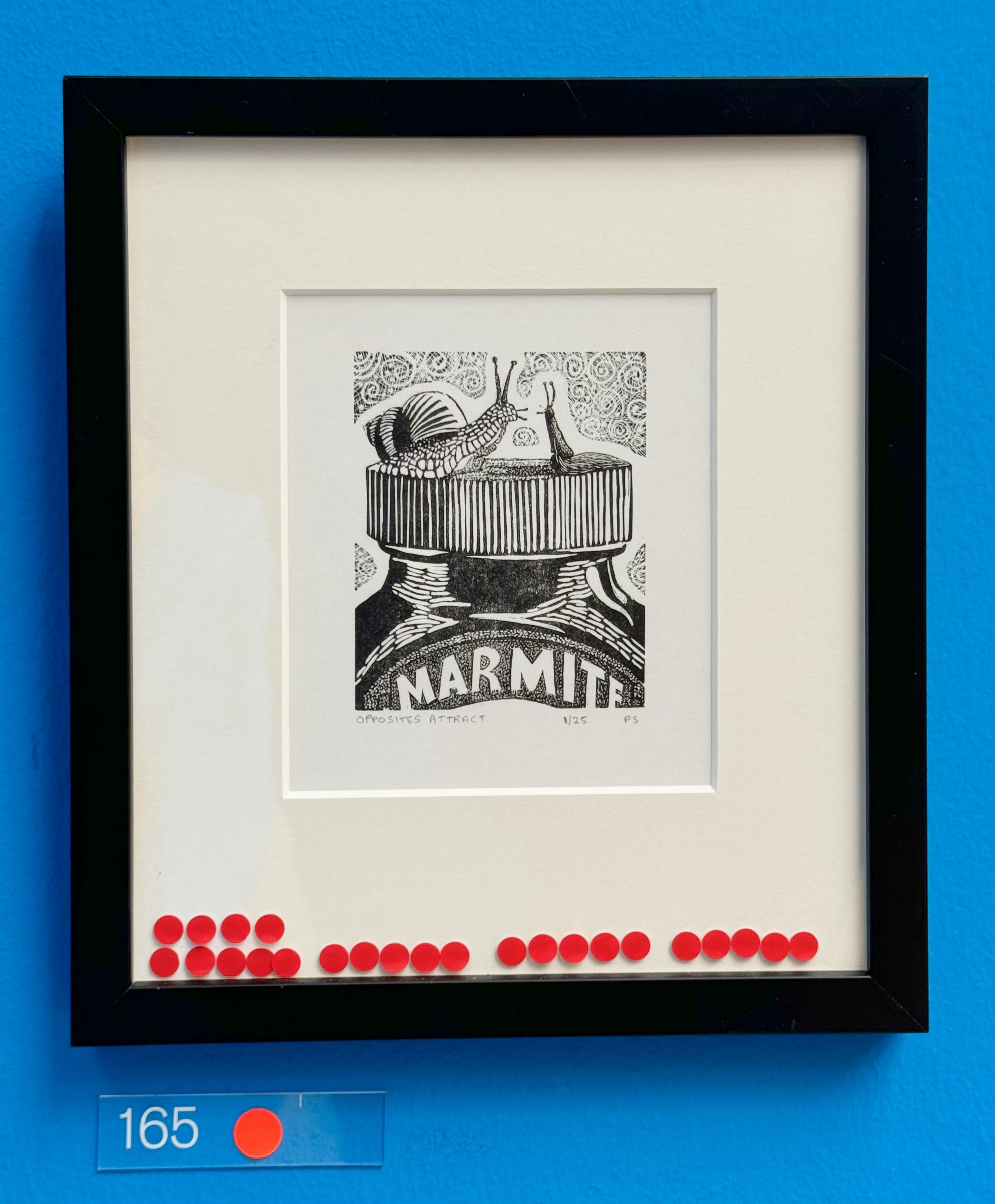 Framed black-and-white wood engraving artwork of a snail and slug on a marmite jar, titled “Opposites Attract,” displayed against a blue wall.
