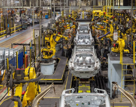 Automated automotive assembly line with yellow robotic arms welding and assembling unfinished car bodies.