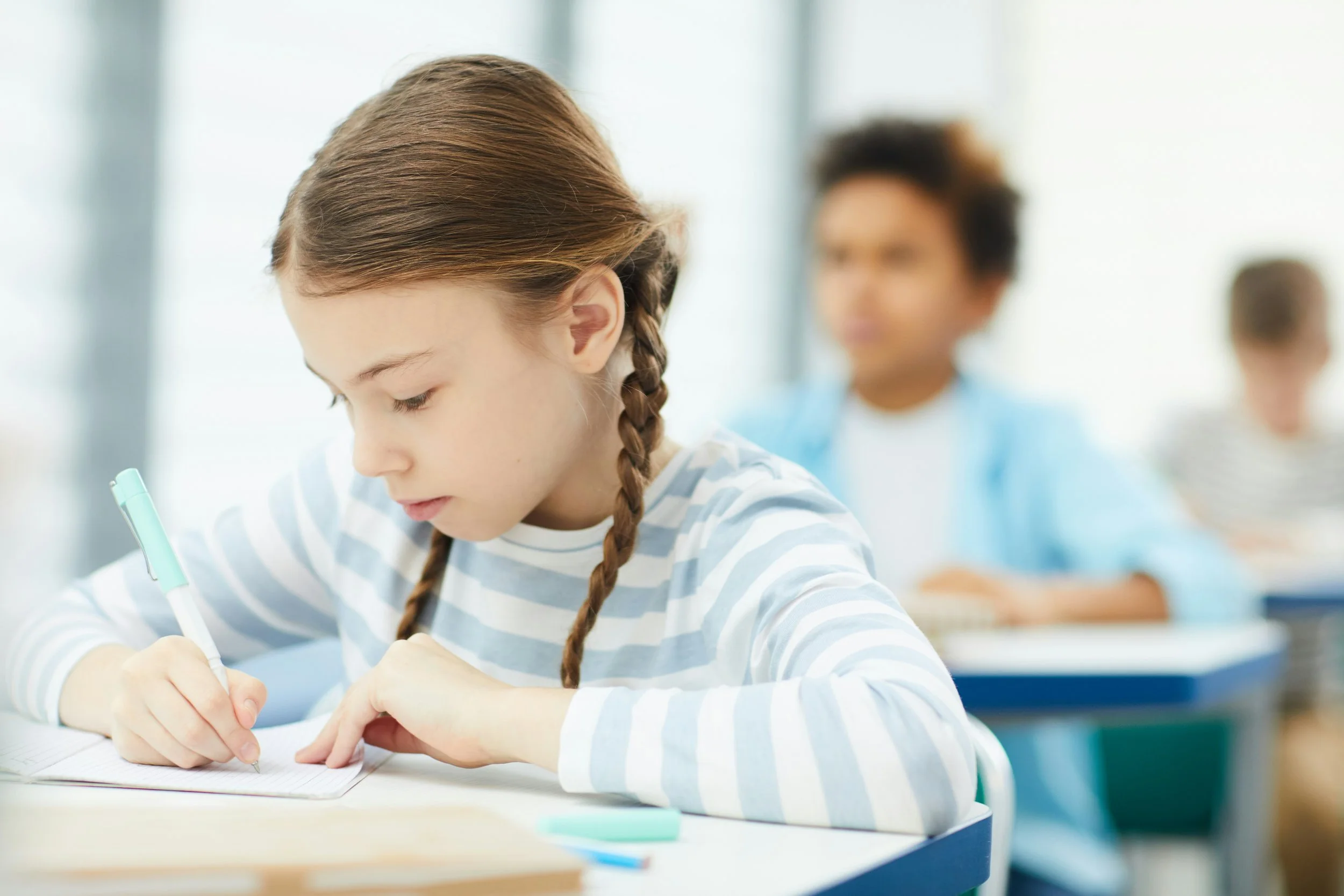 Schoolgirl with braided hair writing in a notebook at her desk in a classroom