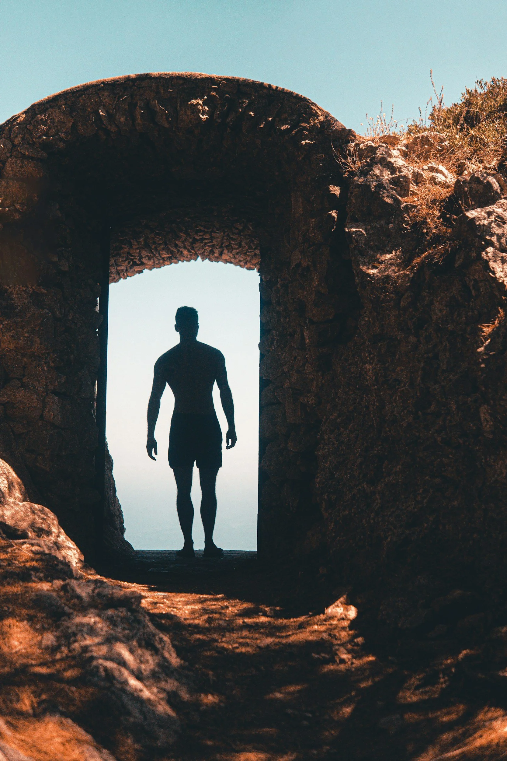 A silhouette of a person standing inside a stone archway with a clear sky in the background.