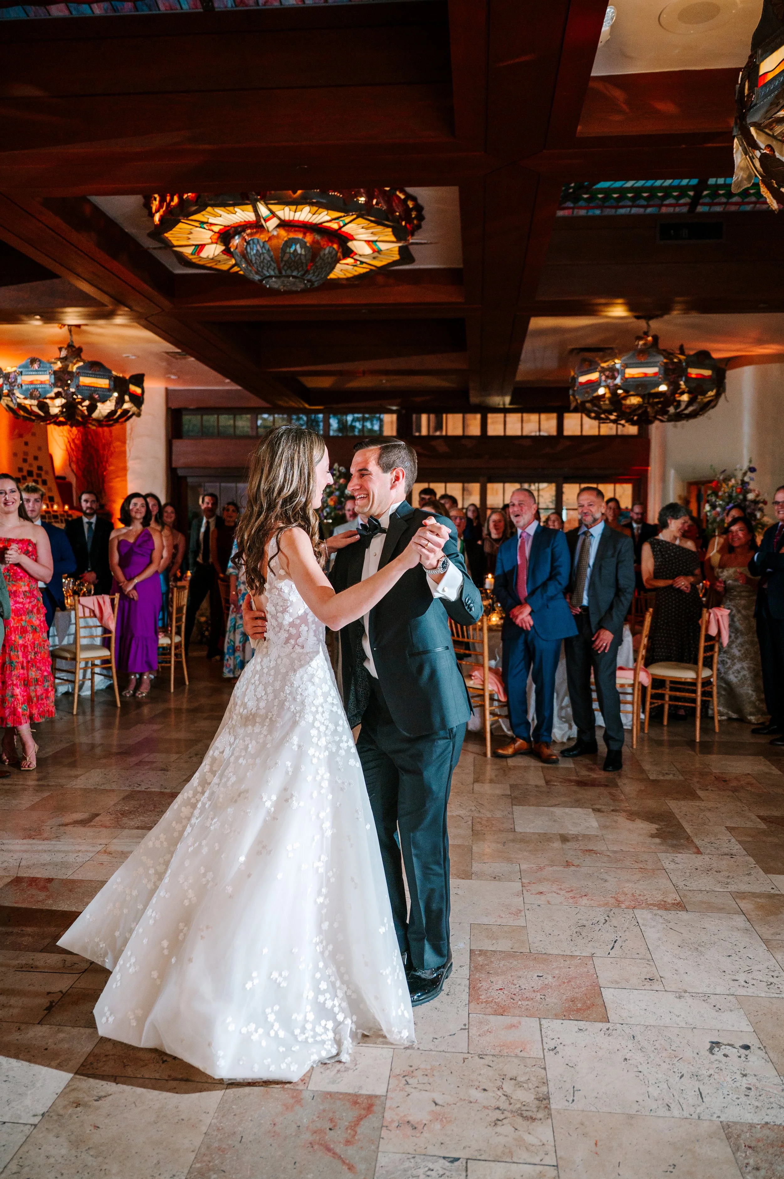 Bride and groom dancing together as wedding guests watch in an ornate reception room