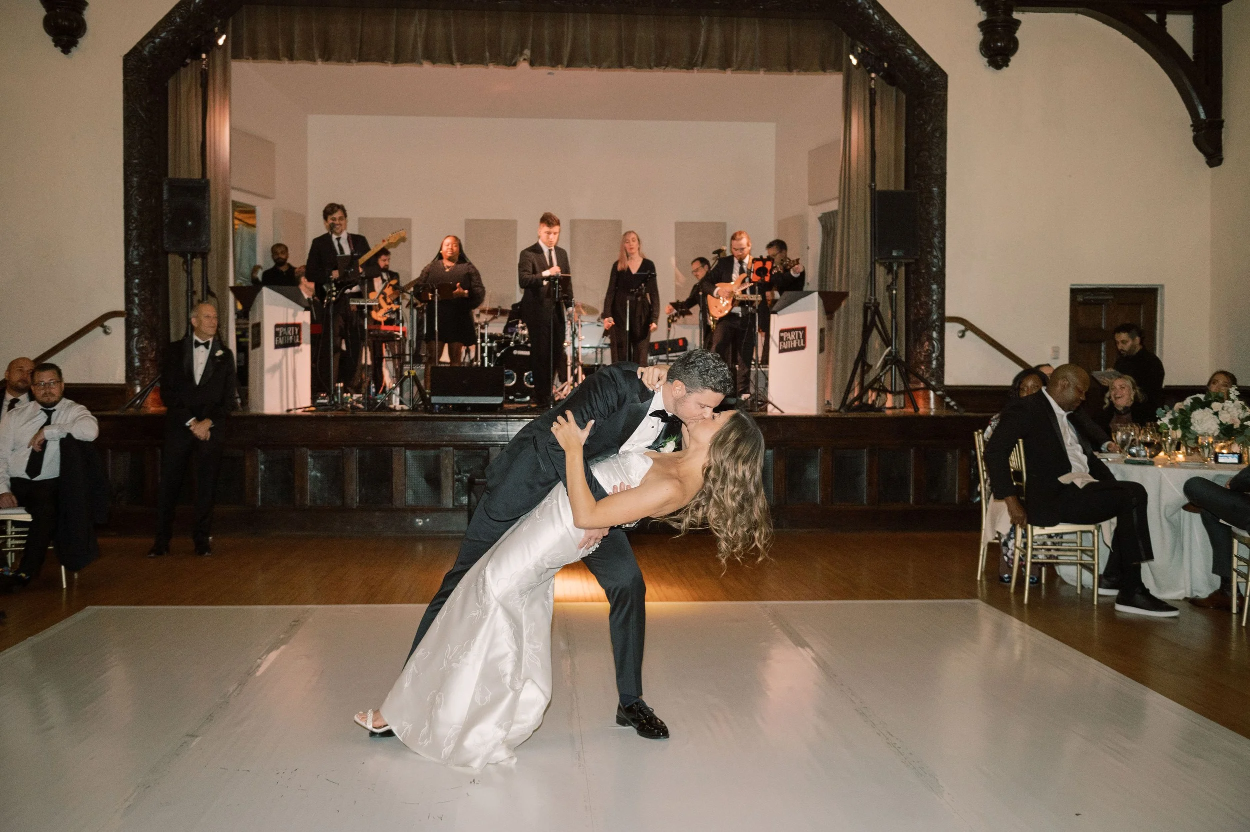 Groom dipping his bride on the ballroom dance floor while wedding guests watch
