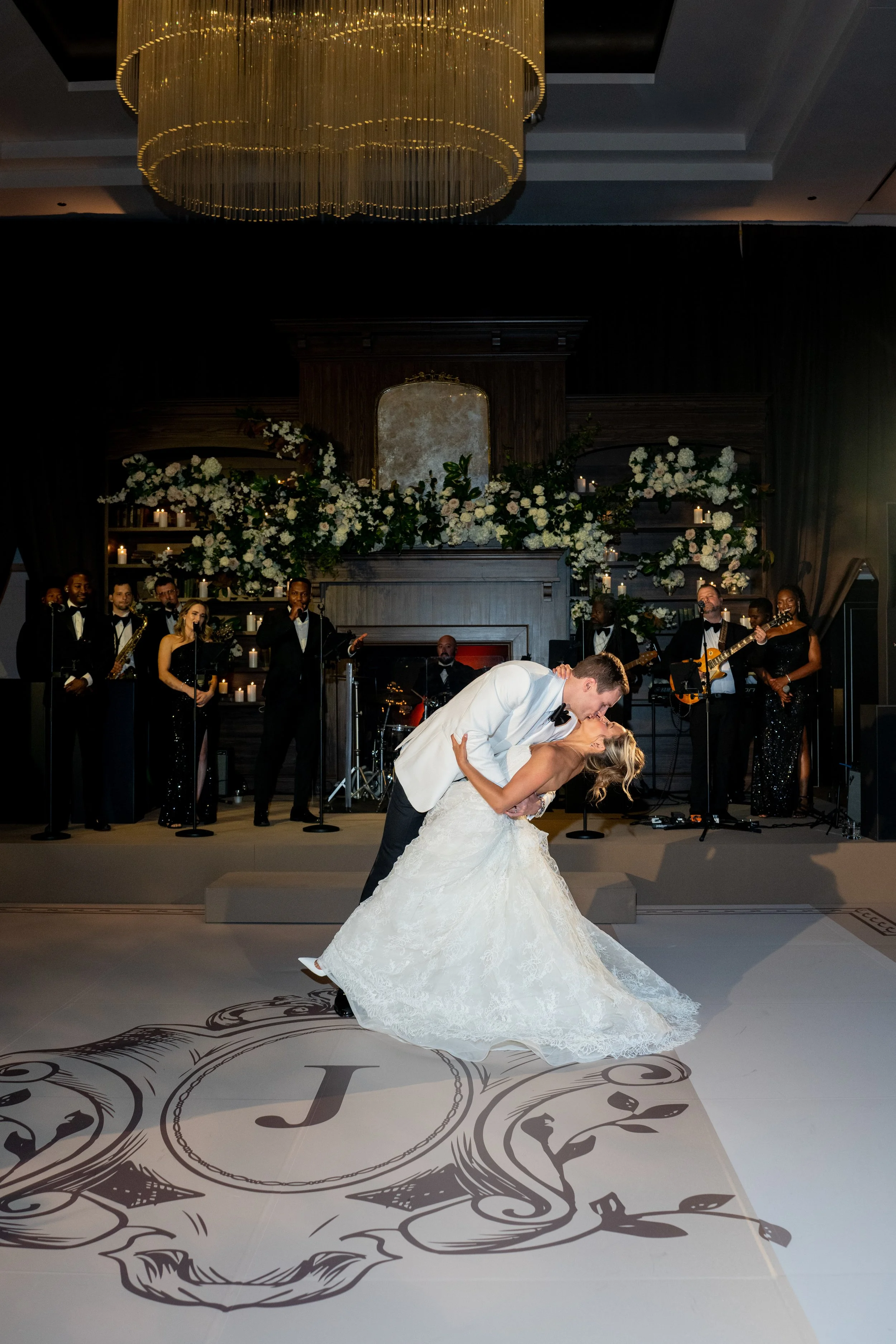 Bride and groom sharing a first-dance dip on a monogrammed dance floor beneath a chandelier