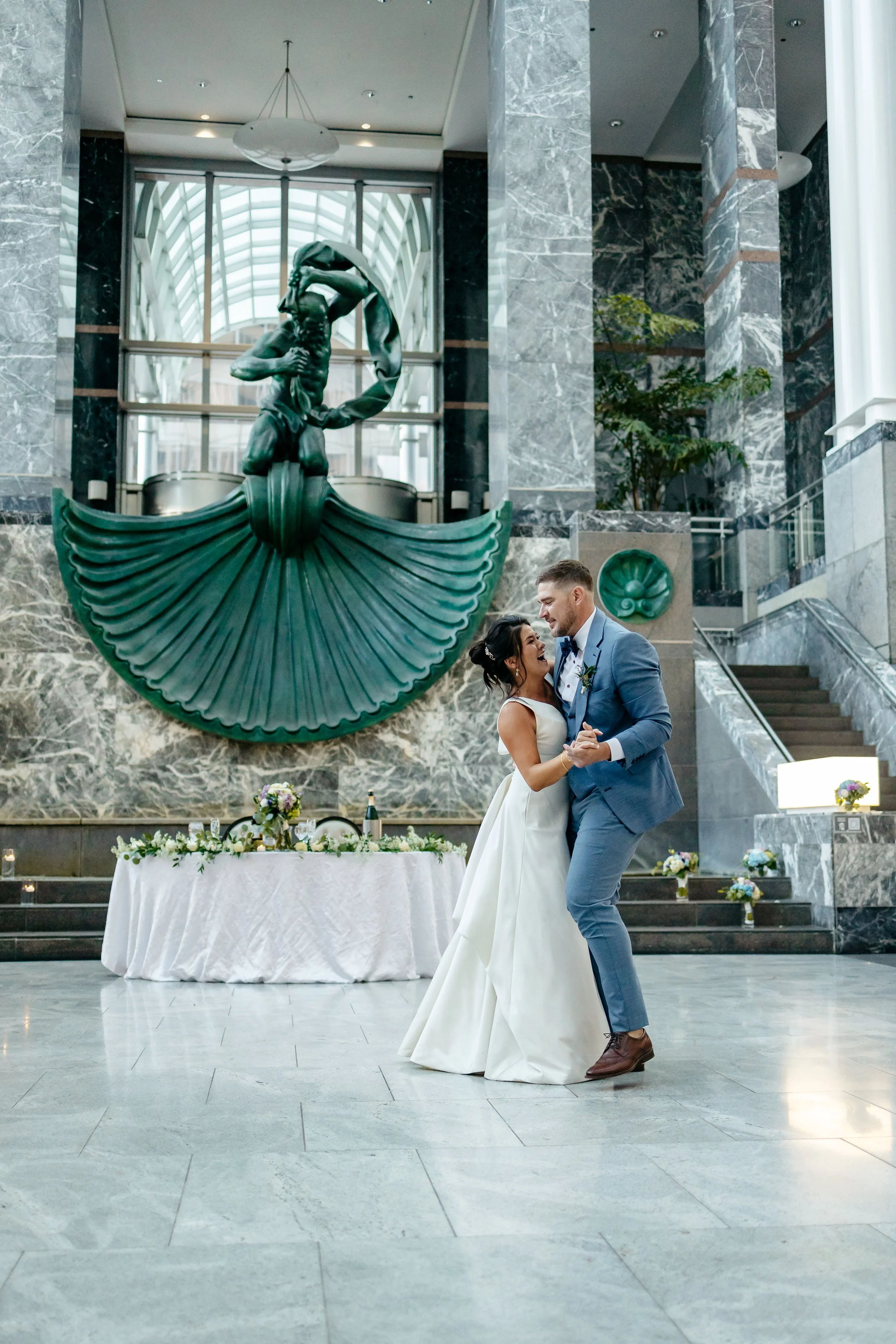 Bride and groom in a blue suit dancing beside an ornate green staircase
