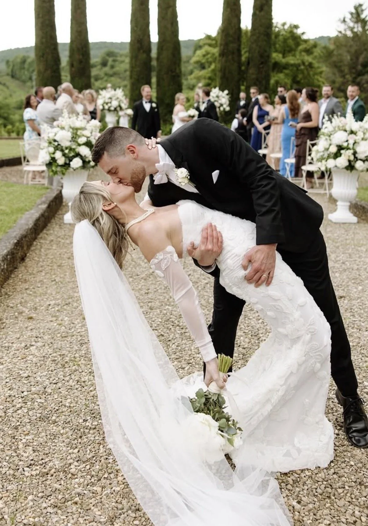 Groom dipping his bride outdoors beside flowering garden plants
