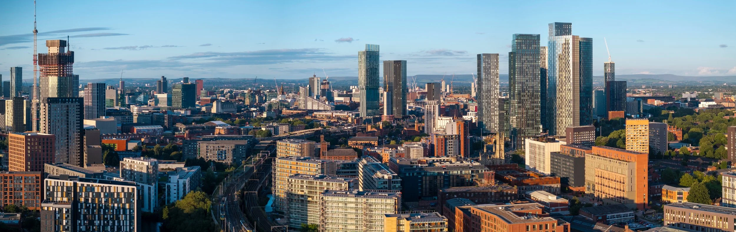 Skyline of a modern city with tall skyscrapers, some under construction, and a mix of residential and commercial buildings, with a clear blue sky.