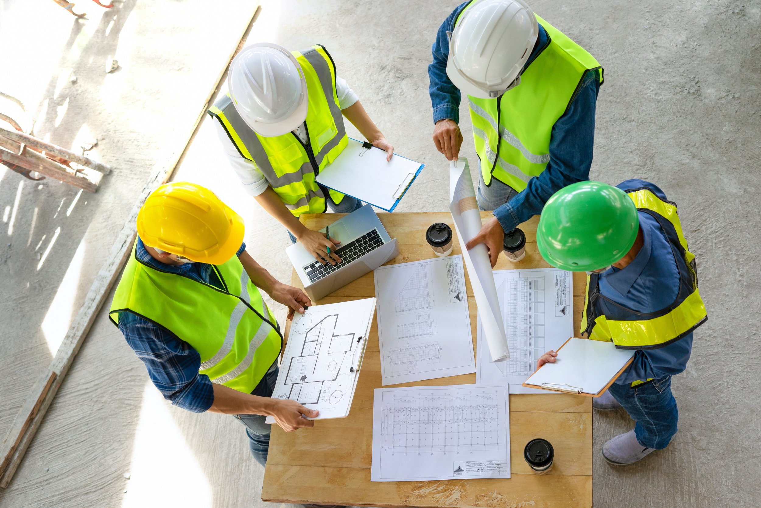 Group of construction workers wearing safety vests and helmets working on building plans at a construction site.