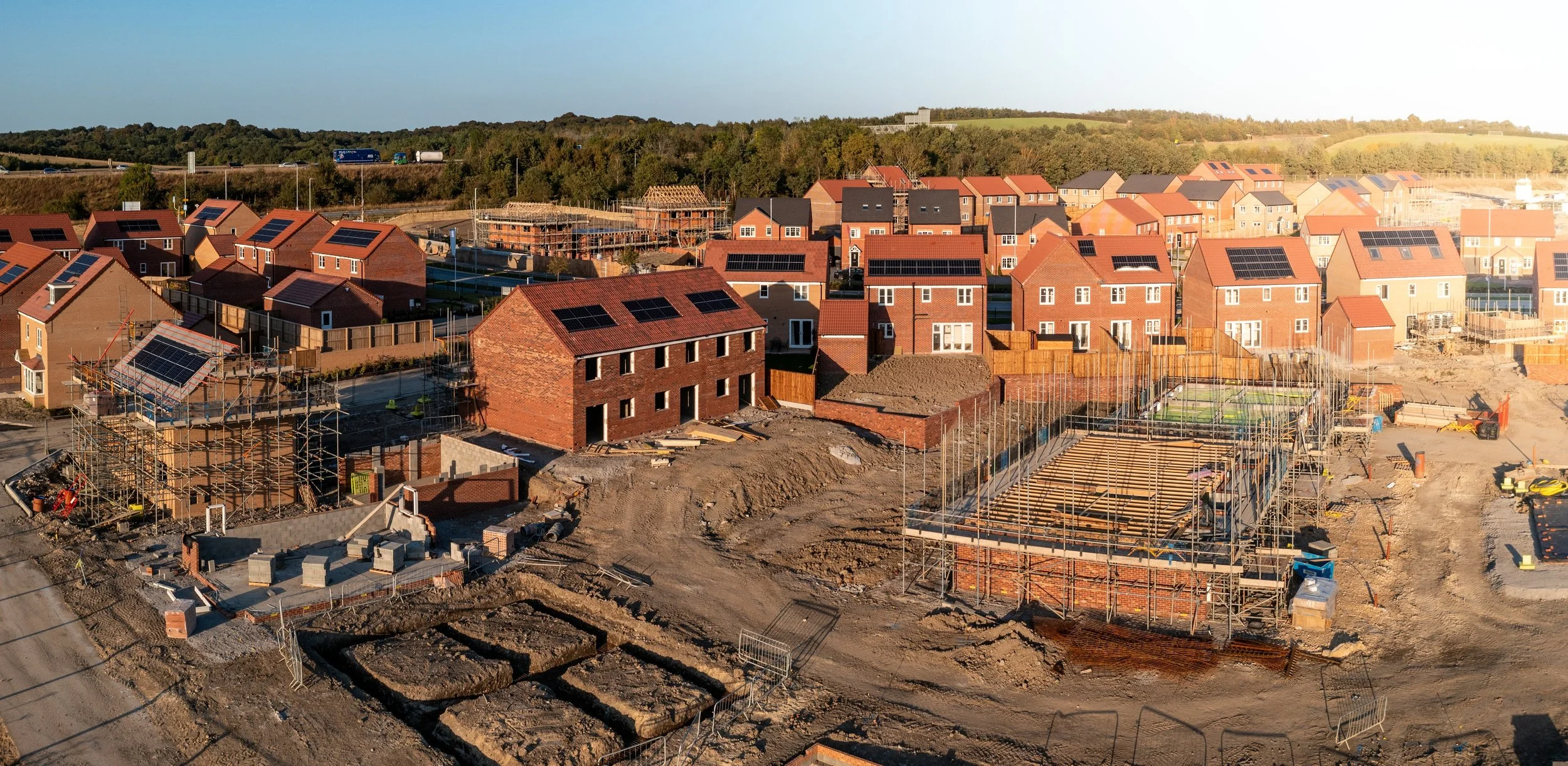 Construction site with partially built houses, scaffolding, and ongoing building work in a suburban neighborhood.