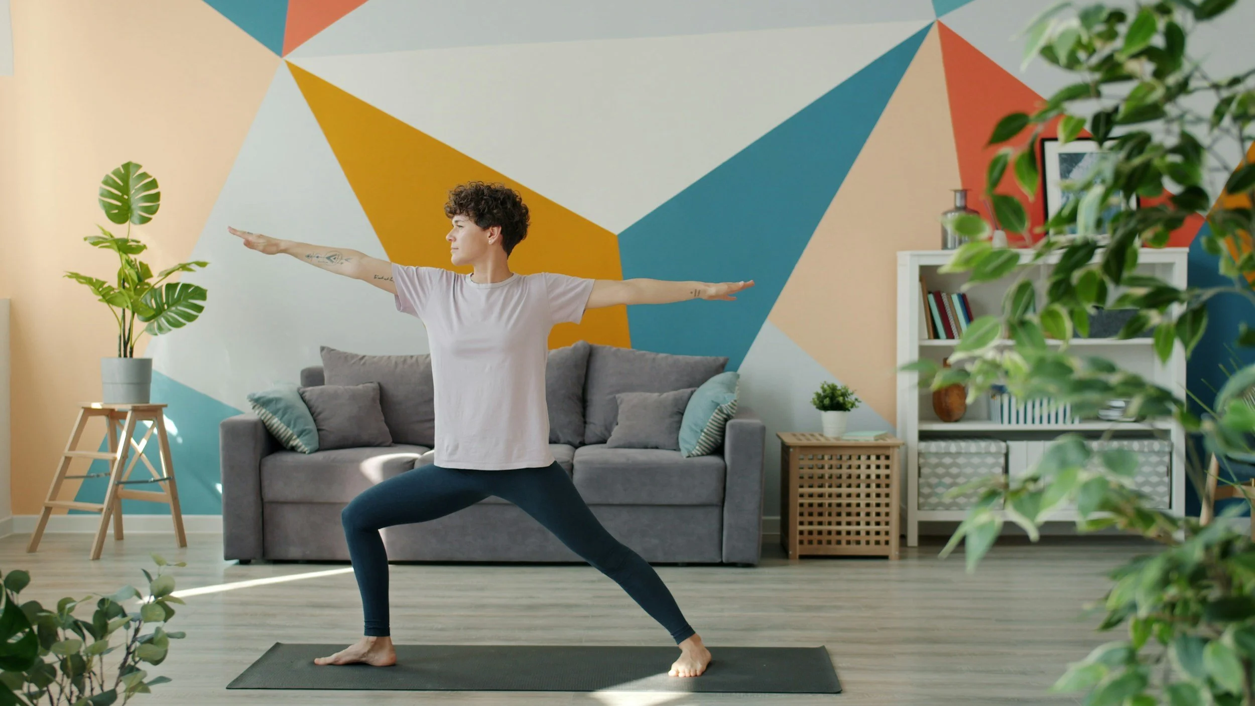 Person practicing yoga in a living room with colorful geometric wall art, plants, and furniture.