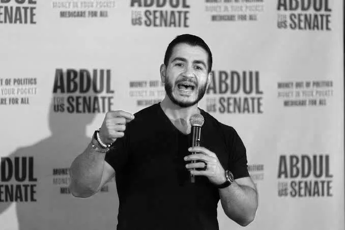 Man speaking into a microphone at a campaign event for Abdul for Senate, with campaign posters in the background.