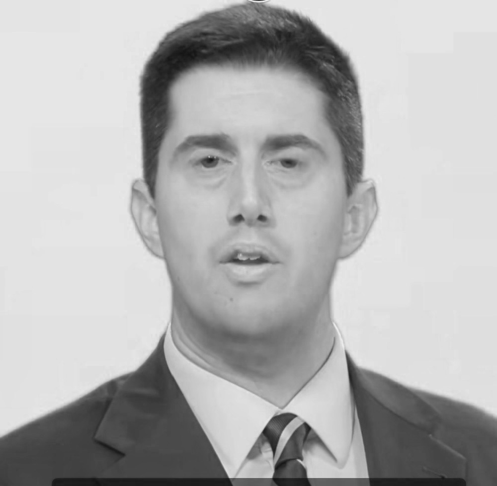 Black and white photo of a man in a suit and tie, speaking